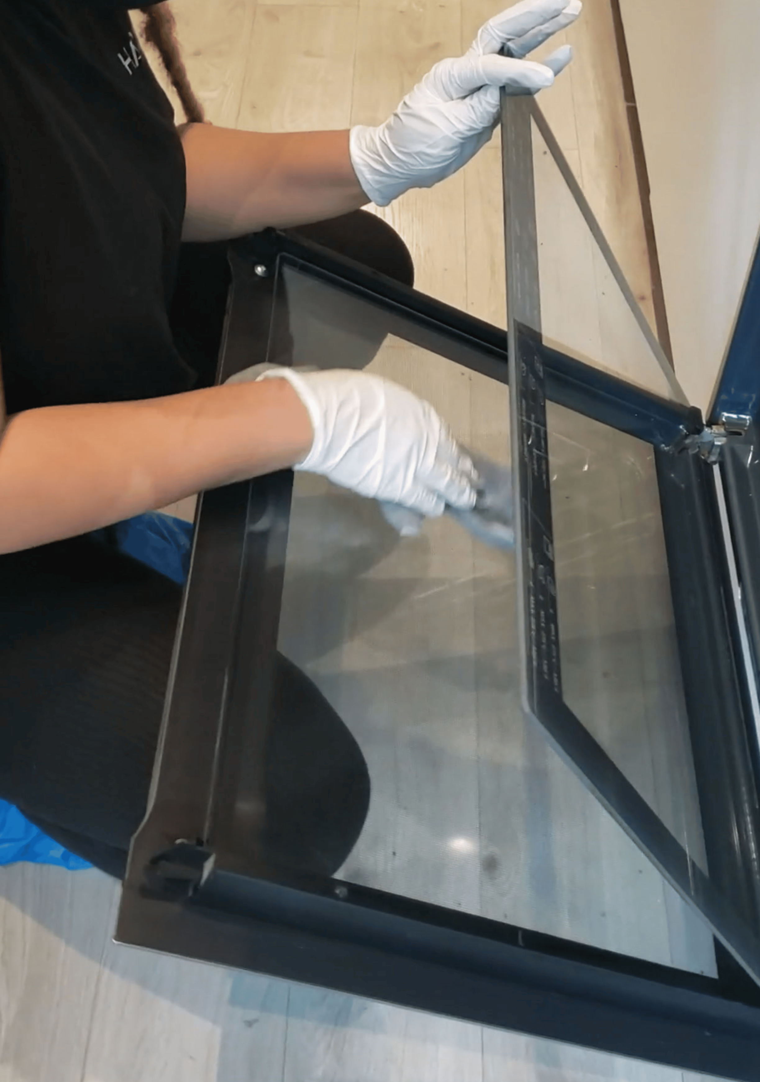 Person wearing white gloves deep cleaning a glass inside oven.