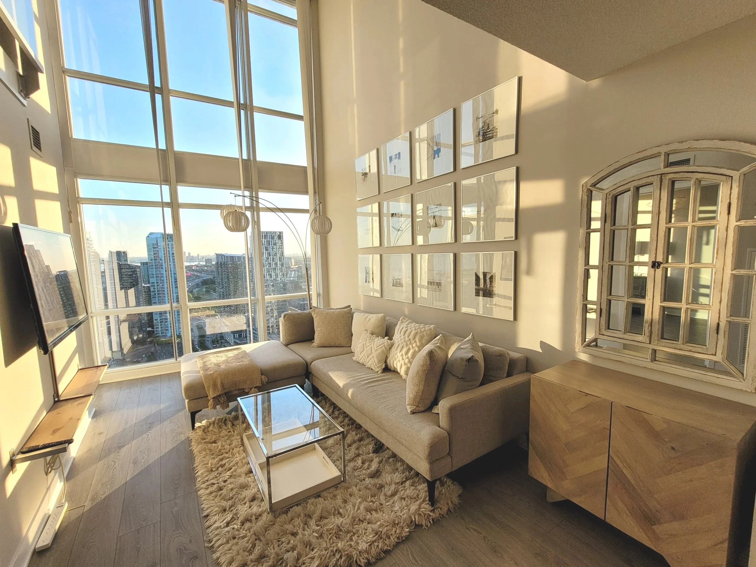 Clean sunlit modern living room with large floor-to-ceiling windows and Cityplace Toronto skyline view.