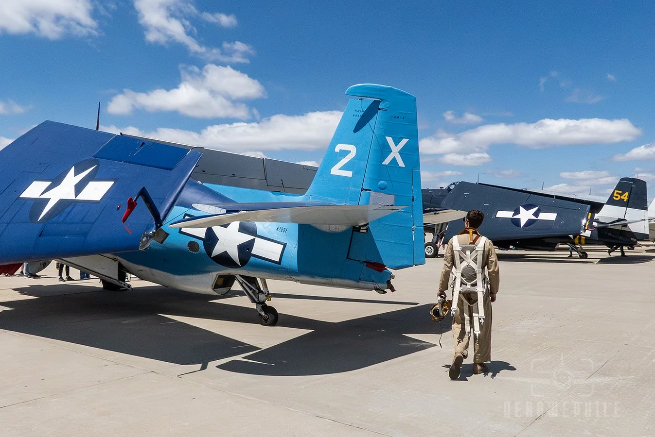 Reenactor in WWII period flight uniform walking around a TBM-3E Avenger