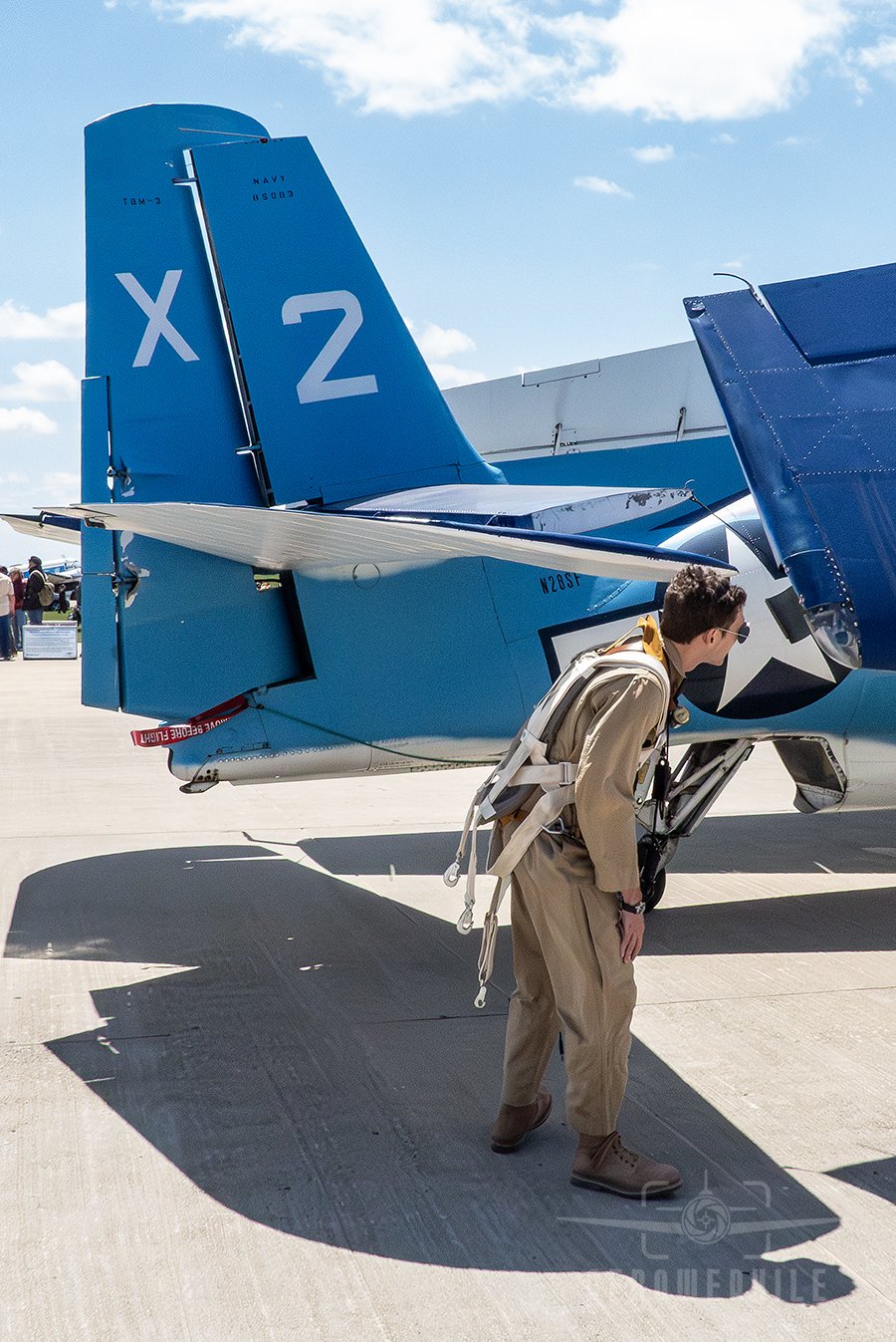 Reenactor in WWII period flight uniform walking around a TBM-3E Avenger