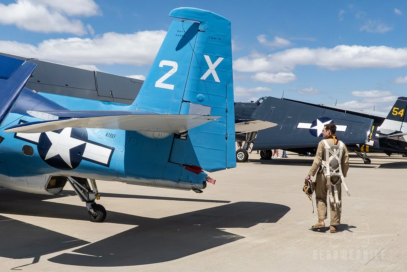 Reenactor in WWII period flight uniform walking around a TBM-3E Avenger