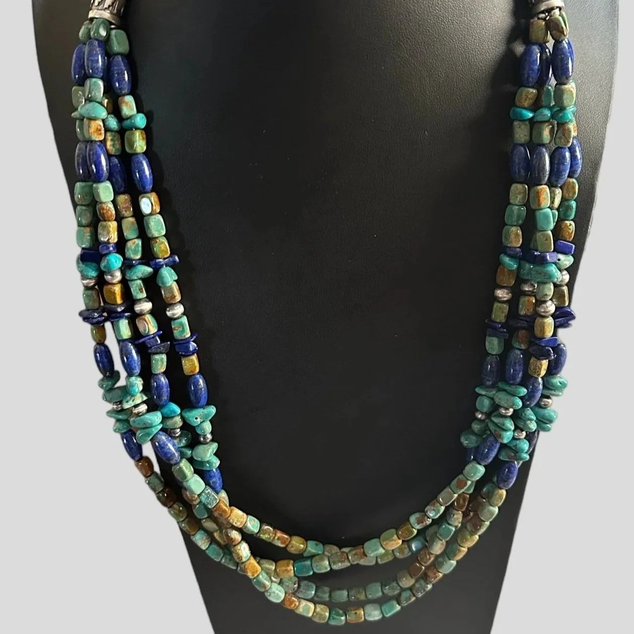 Multi-strand beaded necklace with blue, turquoise, and mixed-colored beads displayed on a black necklace stand. The text 'Victoria's Southwest Designs' is written in blue cursive at the bottom of the image.