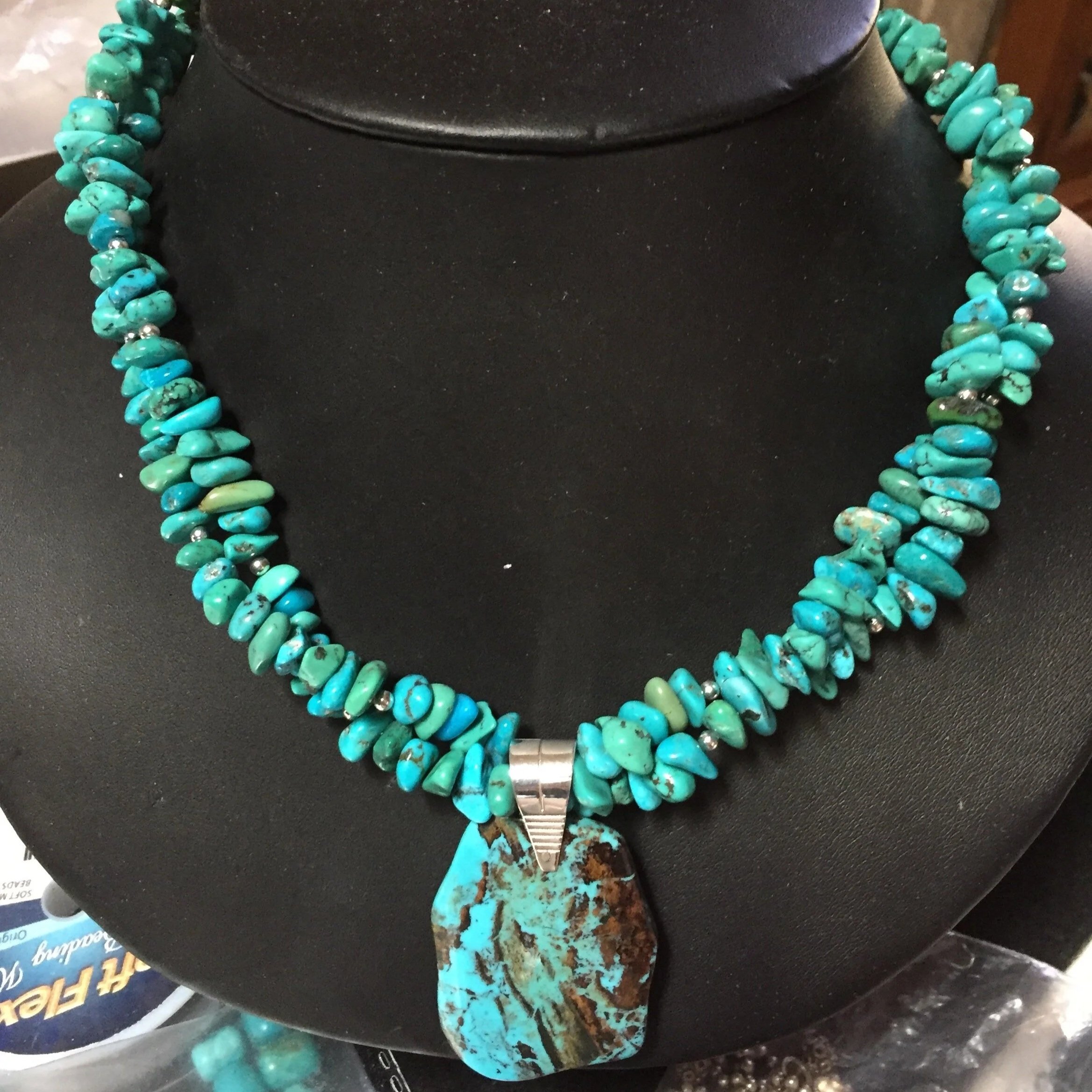 Turquoise and silver beaded necklace with a large turquoise pendant on a black display bust.