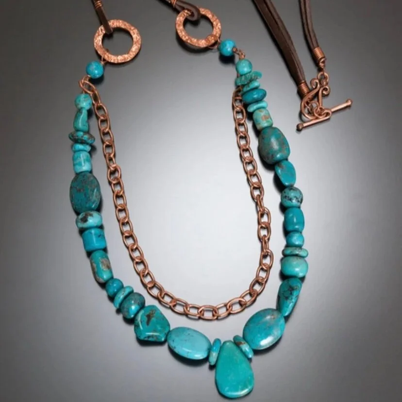 Two turquoise beaded necklaces with copper chains and leather cords on a gray background.