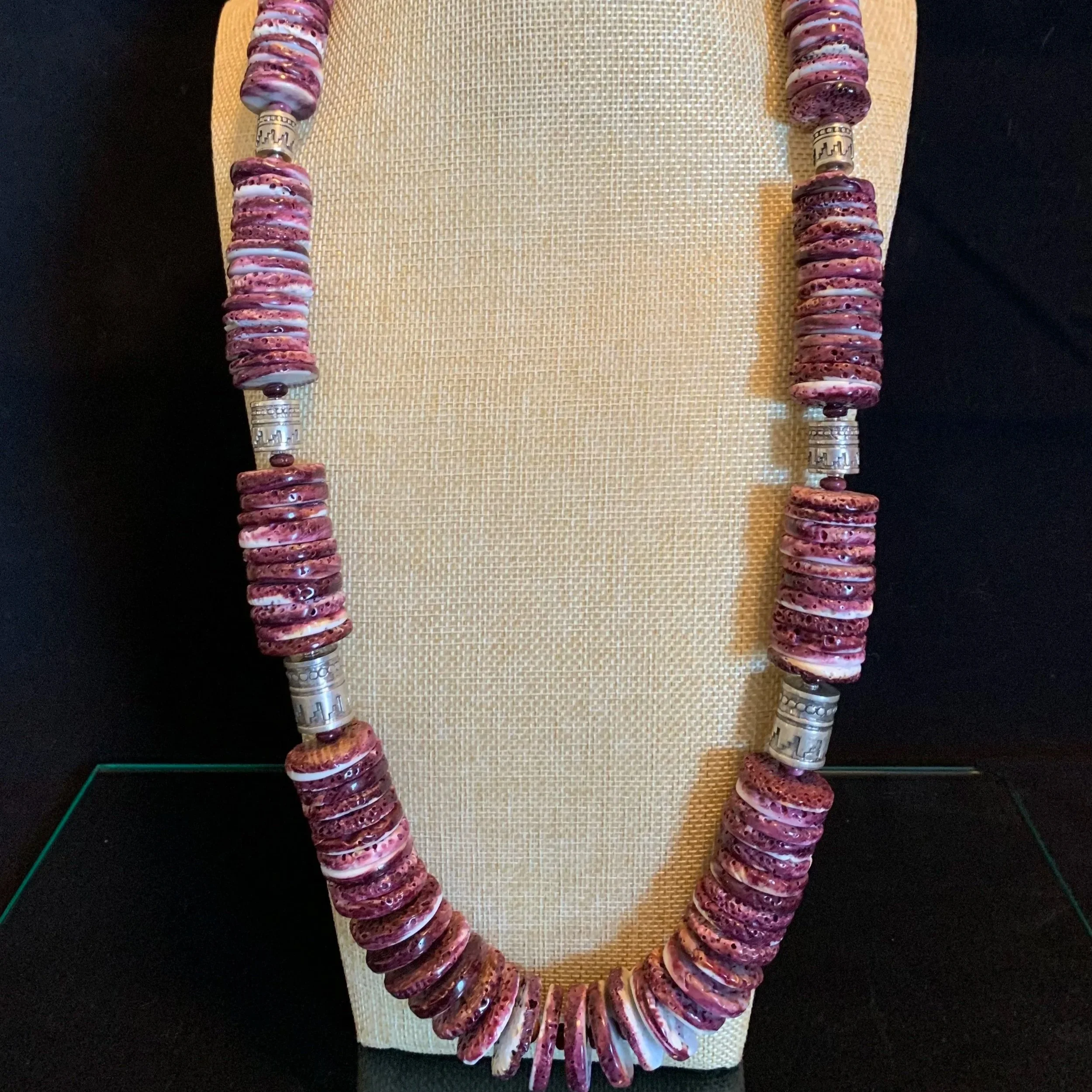 A necklace made of large pink and purple ceramic beads and silver spacer beads, displayed on a beige bust mannequin.