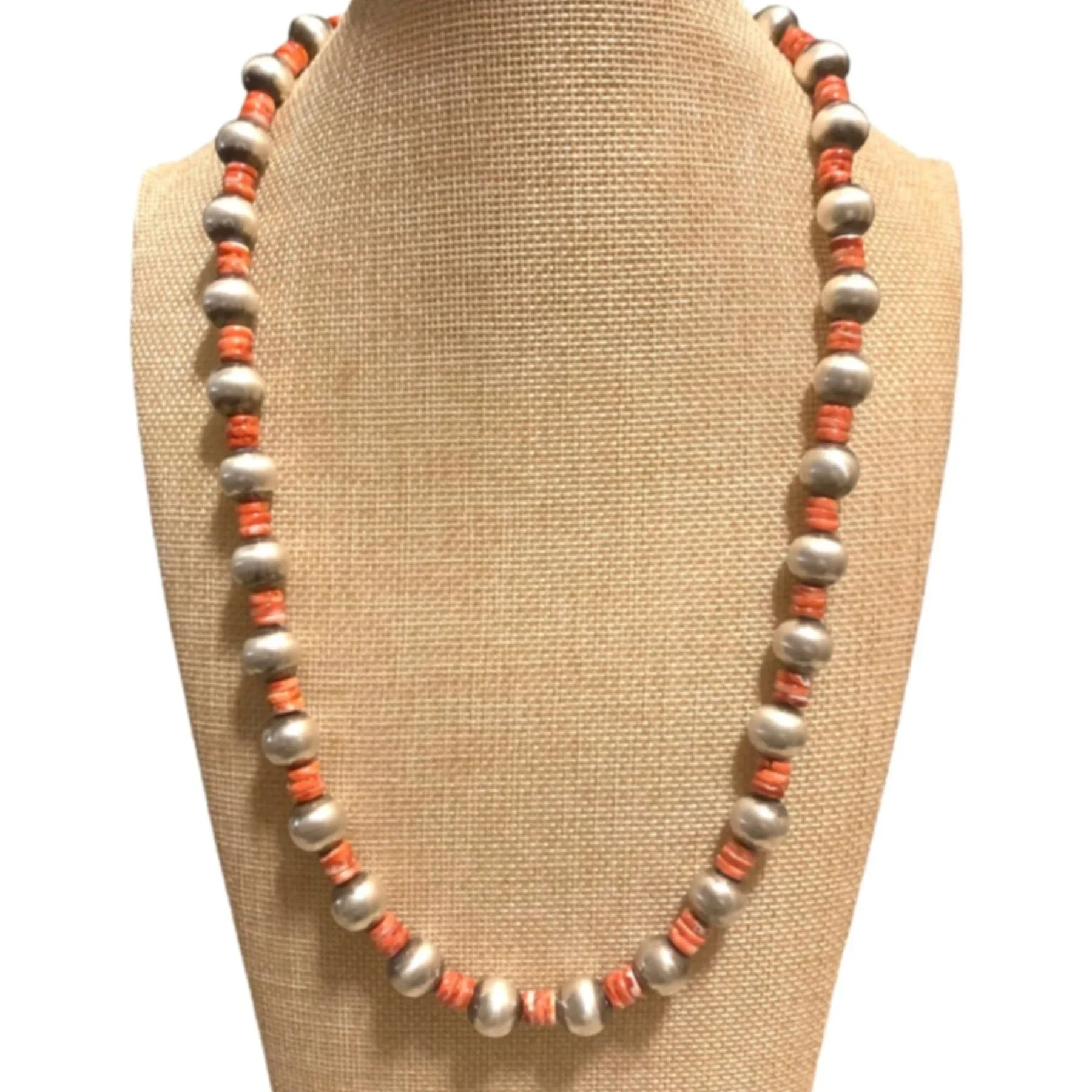 Beaded necklace with gray beads and coral-colored spacer beads displayed on a beige fabric necklace stand.