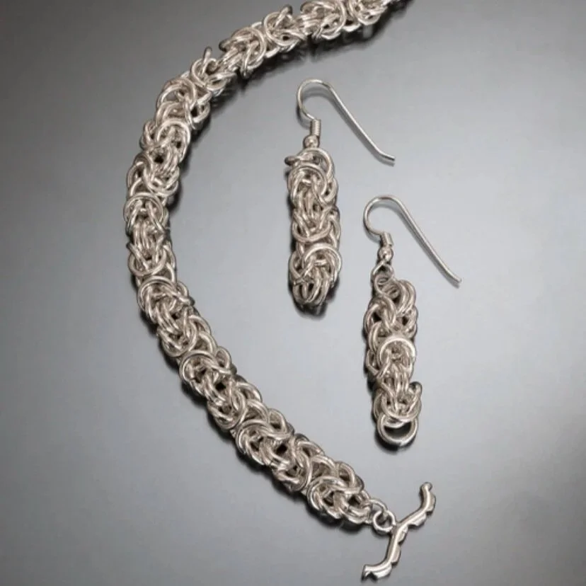 A silver chain necklace and matching earrings on a dark surface.