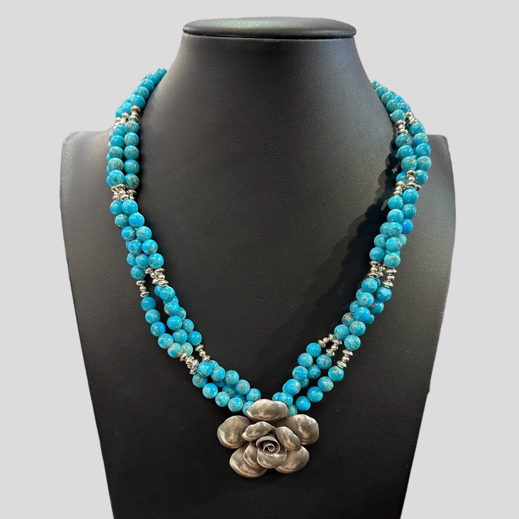 A jewelry display bust with a layered blue beaded necklace and a large metallic flower pendant at the center. The text on the image reads 'Victoria's Southwest Designs' in blue.