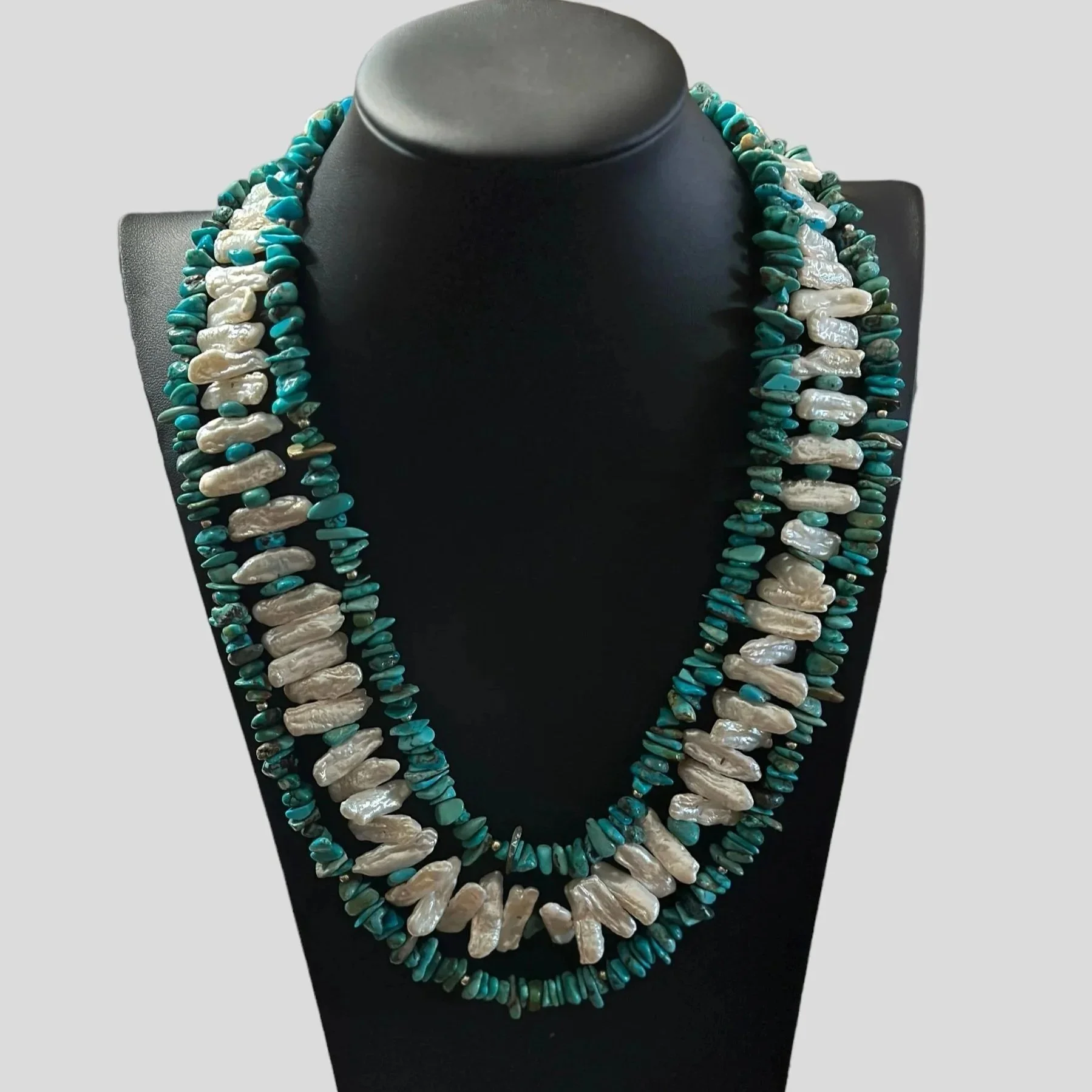 Turquoise and white mother-of-pearl necklace displayed on a black jewelry bust.