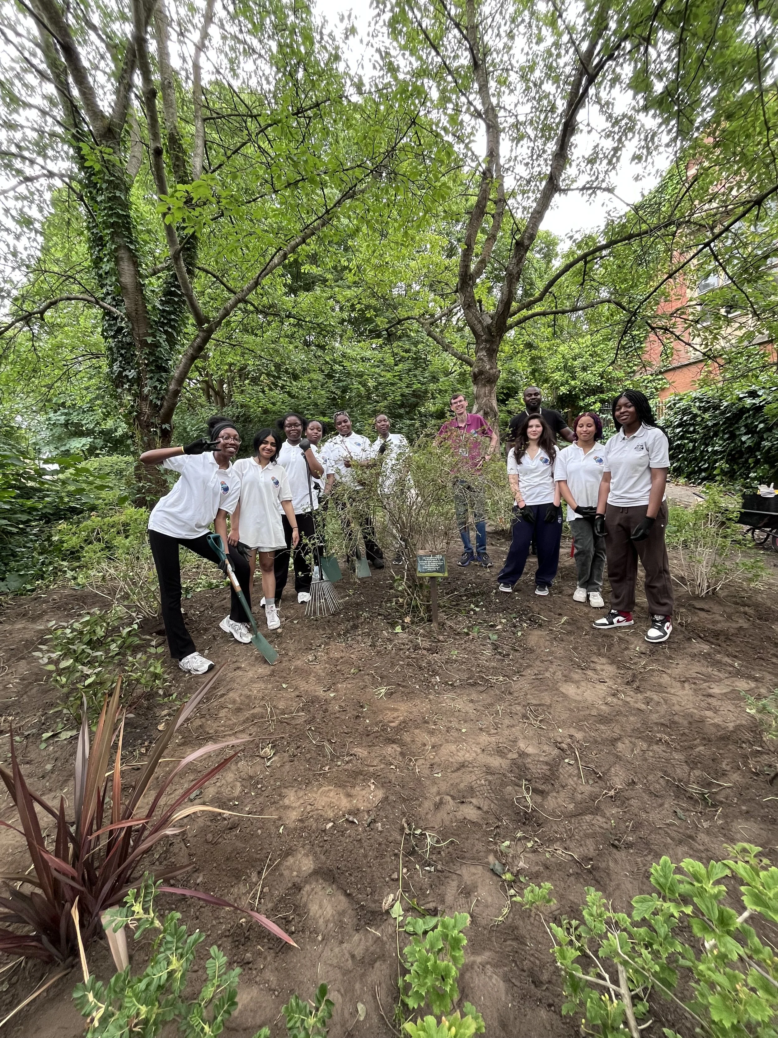 9 St Ursula's students pose around a freshly cleared garden space with their tools with two adult helpers.