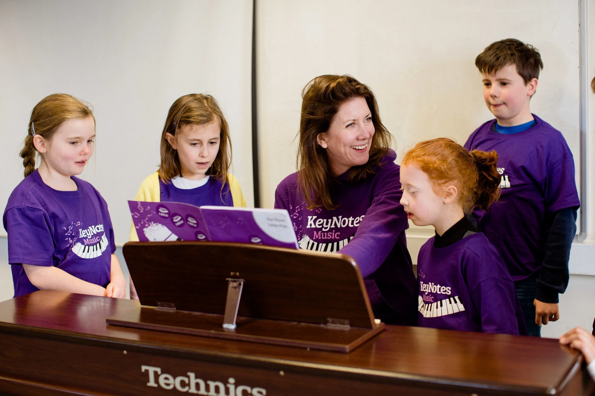 Piano teacher smiling to her students as they follow along with the music book.