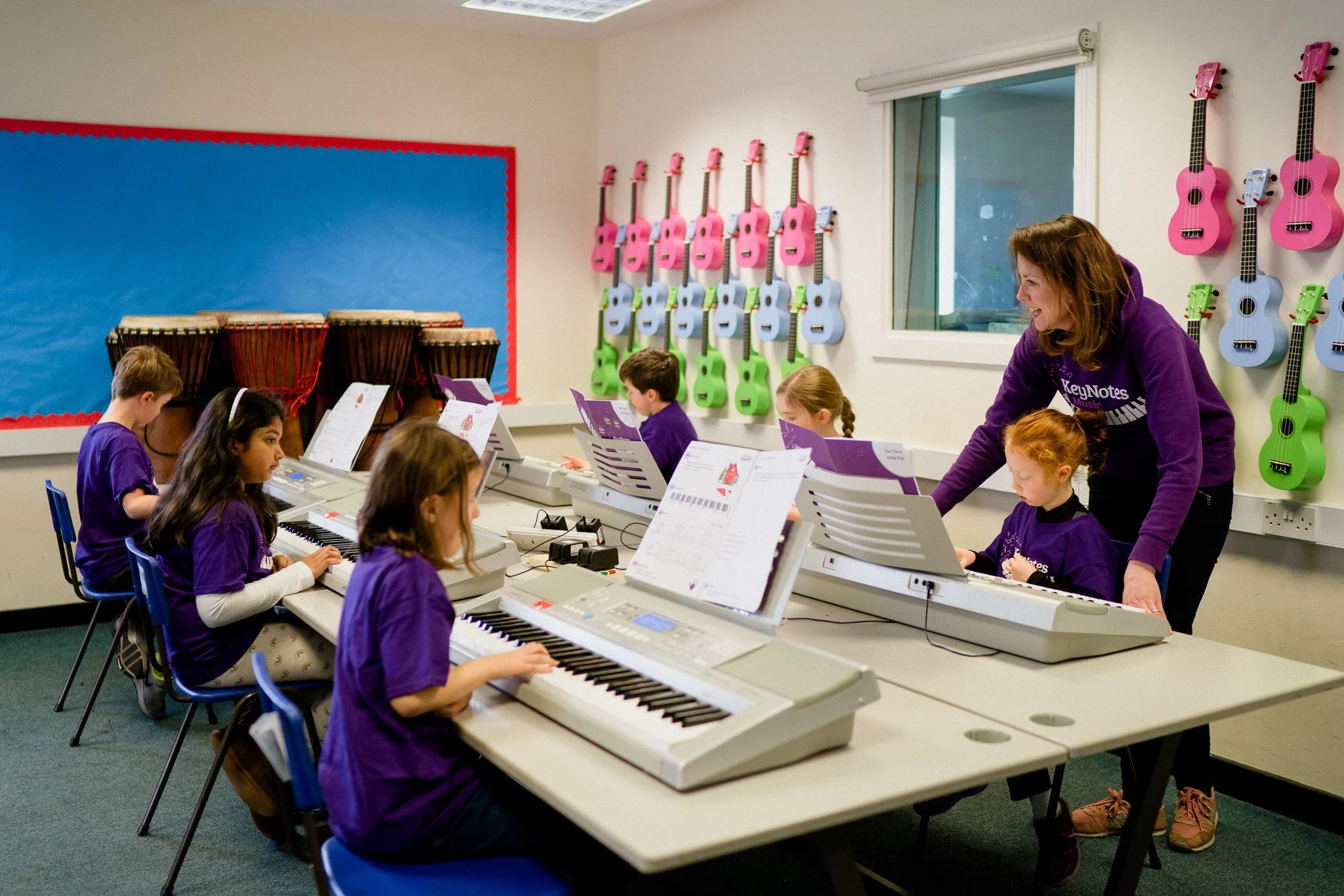 A group of children sit at their digital pianos following notation in their books.