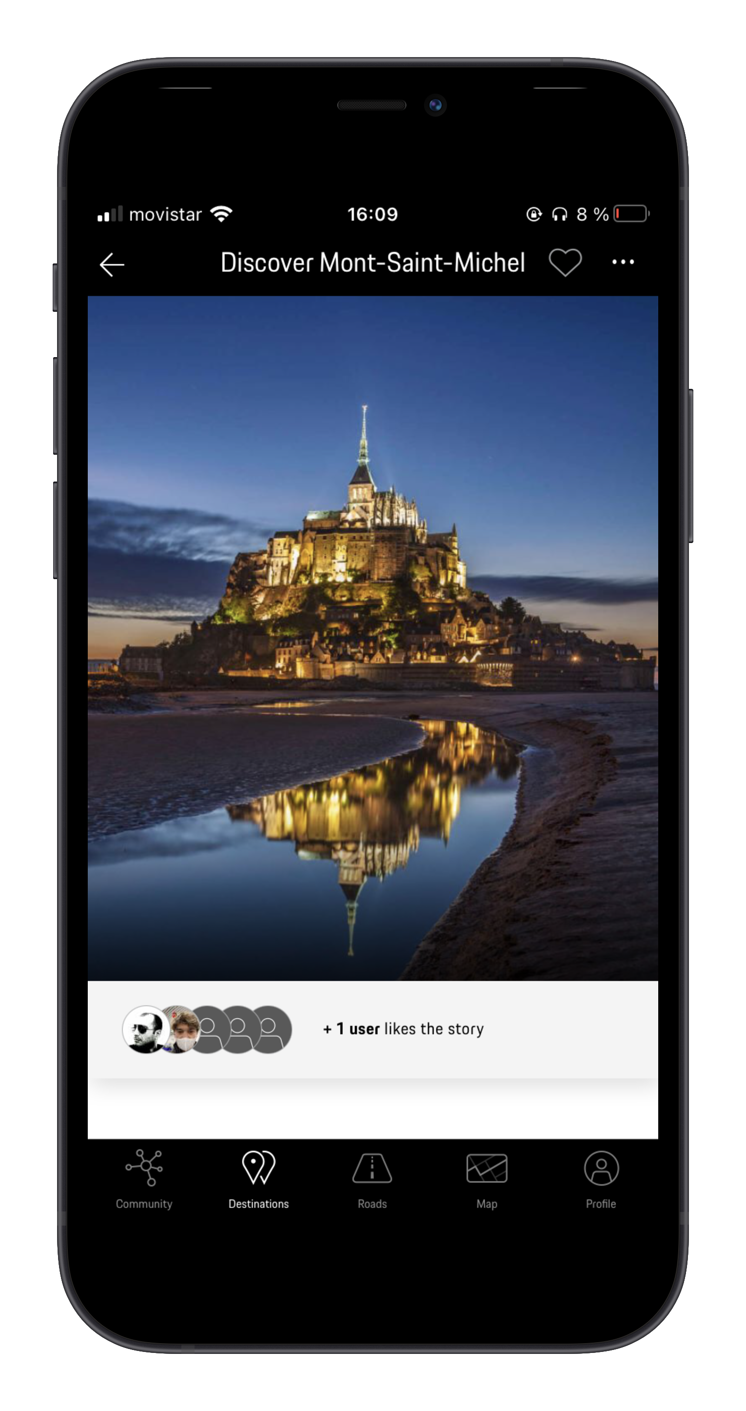 Nighttime view of Mont-Saint-Michel with its illuminated abbey and village, reflected in water on a beach, under a dark blue sky.