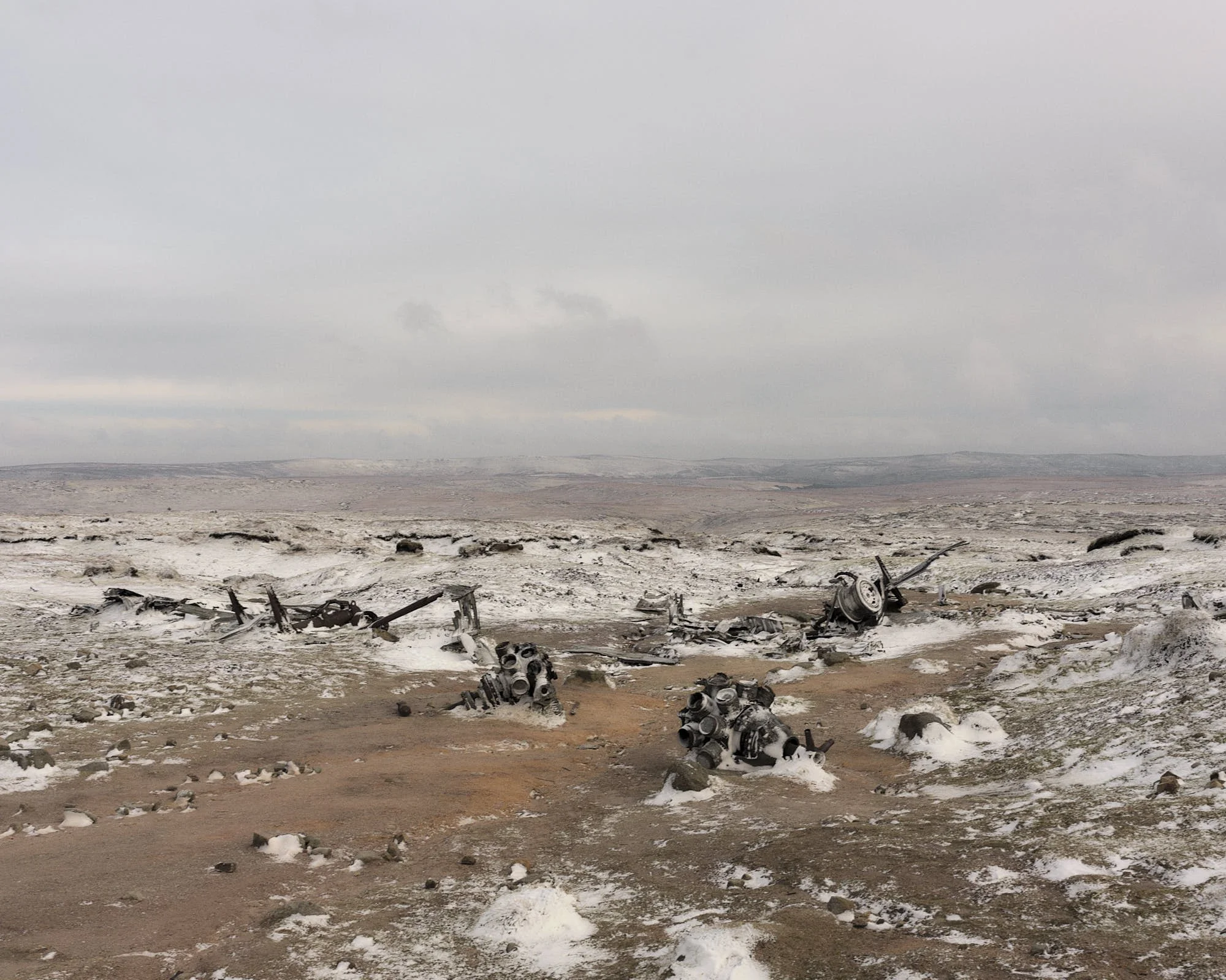 Remains of an aircraft wreckage on a barren, snow-covered landscape under an overcast sky.
