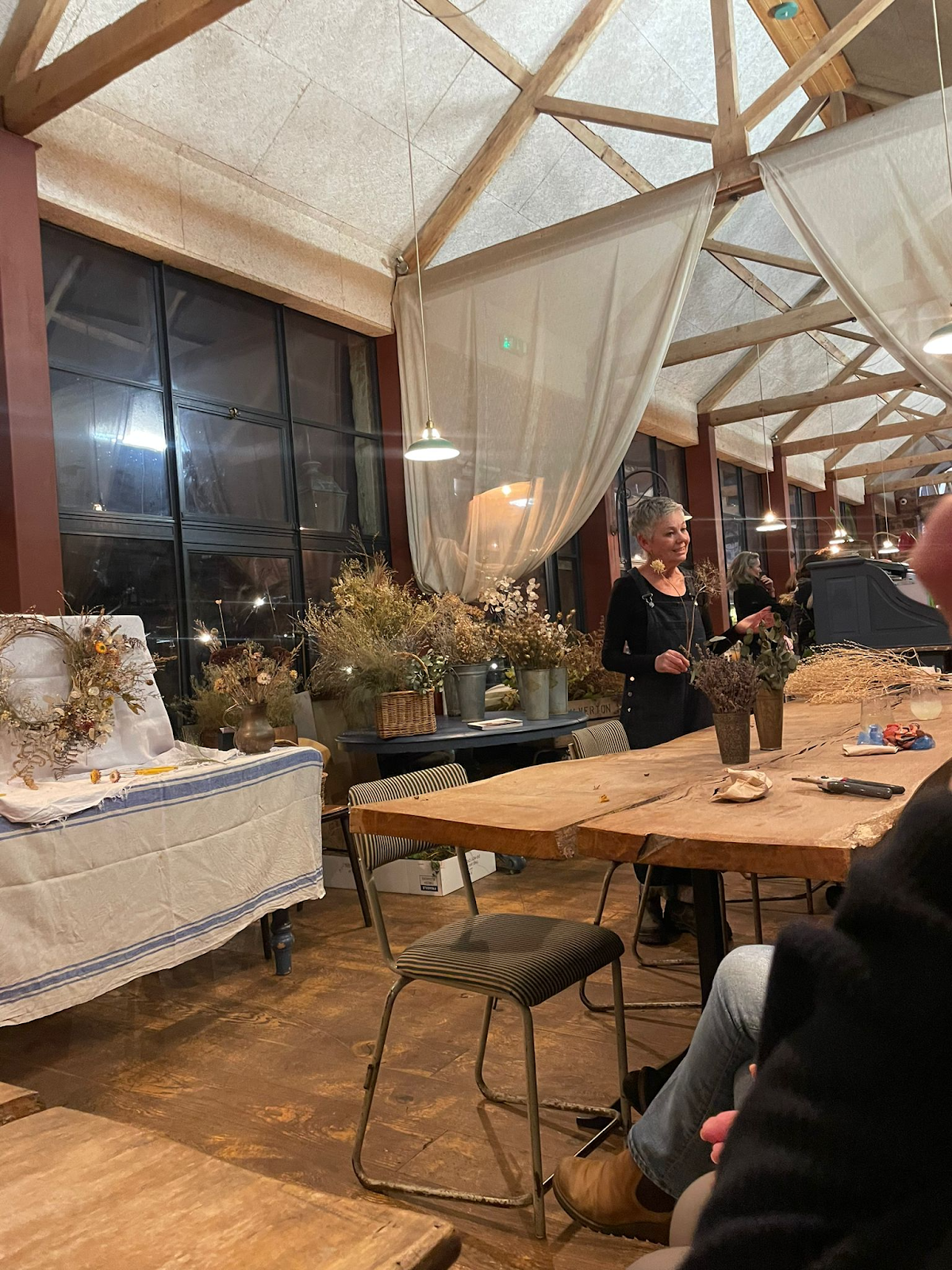 A dried floral arrangement featuring white baby’s breath, beige hydrangeas, purple and green seed pods, and eucalyptus leaves in a circular wicker frame.