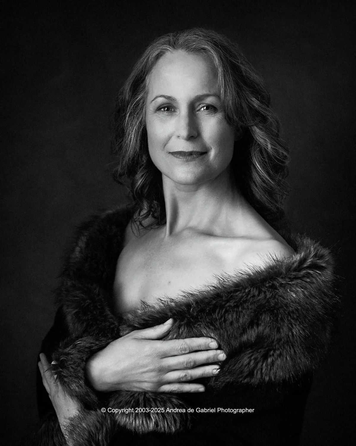 Black and white portrait of a woman with wavy hair, wearing a fur stole, looking confidently at the camera.