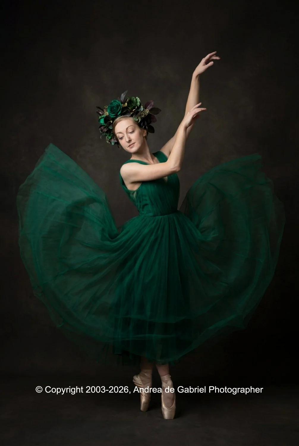 A ballerina in a green dress performing a dance pose with floral headpiece, on pointe shoes, against a dark background.