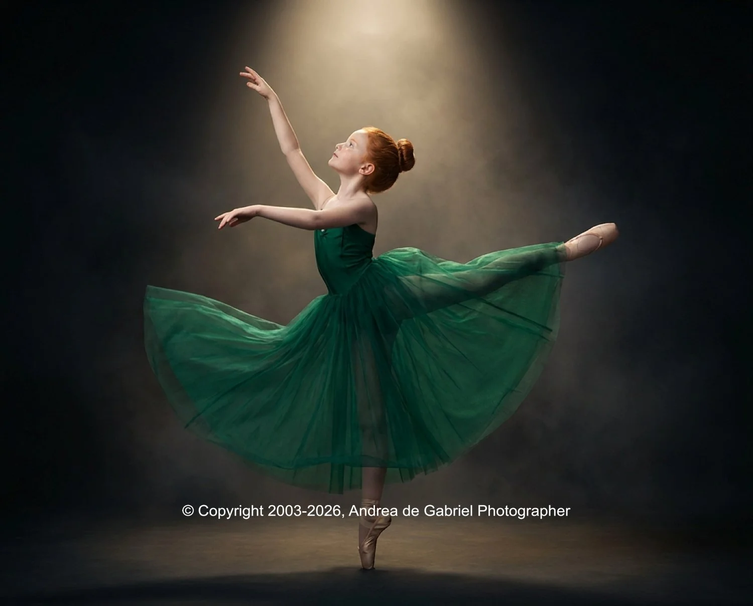 A ballet dancer in a green tutu performing a pose on stage, illuminated by a spotlight.