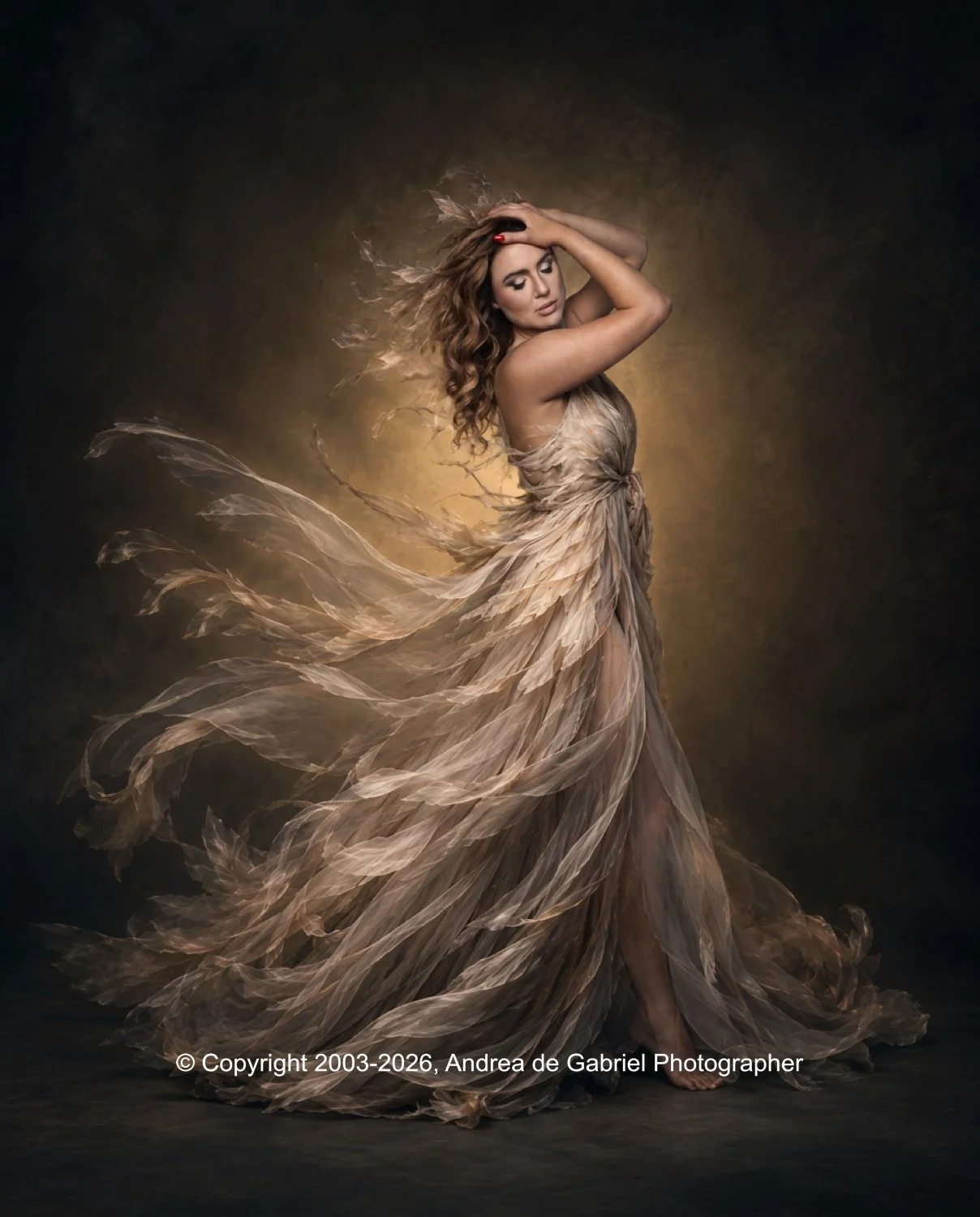 A woman with long, wavy hair wearing a flowing, feather-like beige dress poses with her arms raised and her head tilted to the side, against a dark background with a glow behind her.