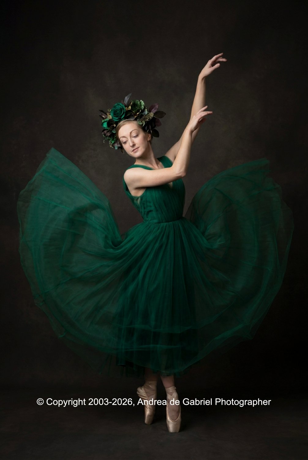 A ballerina in a green dress performing a dance pose with a floral headpiece, standing on pointe against a dark background.