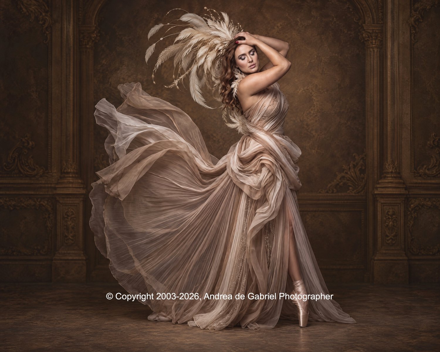 A woman in a flowing, layered, beige gown with a dramatic feathered headpiece poses in a vintage-style room with ornate woodwork and textured walls.