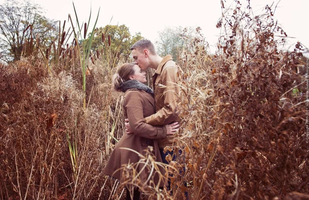 A couple embracing and kissing in a field of tall dry grasses and plants during autumn.