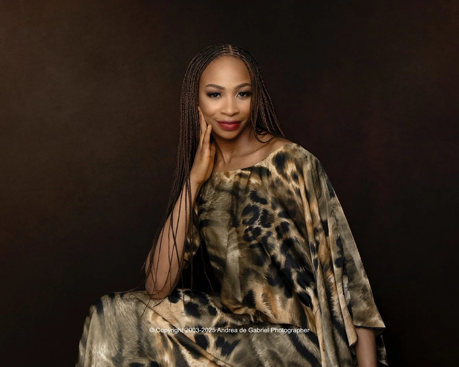 Portrait of a woman with long braids wearing a leopard-print dress, posing against a dark background.