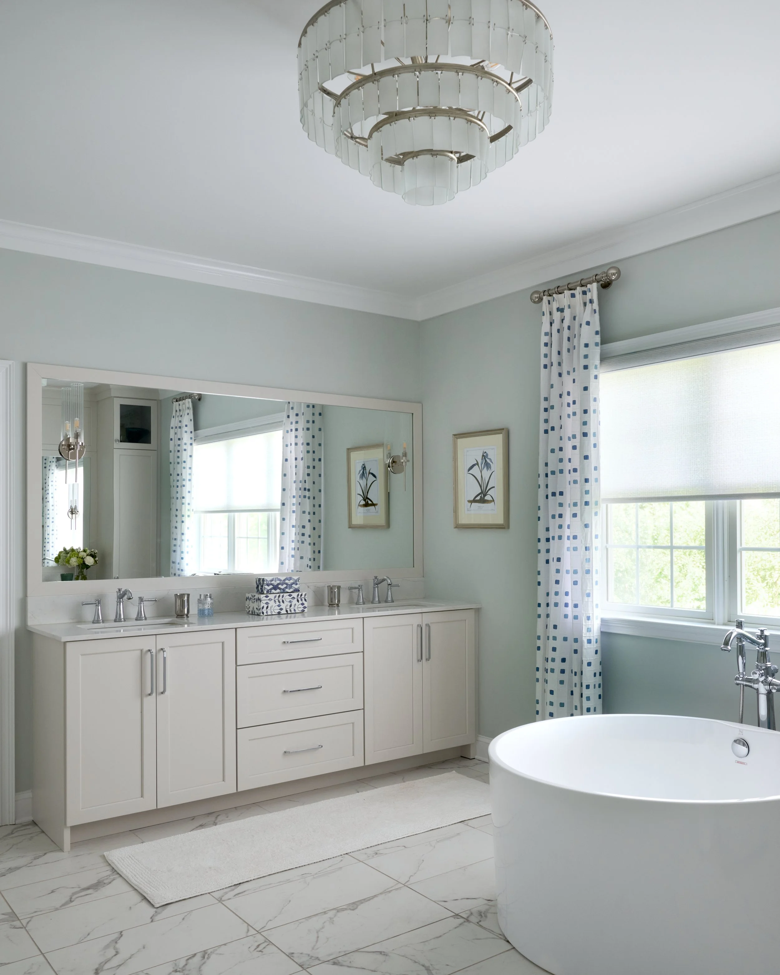 light bright airy clean sleek soothing primary bathroom with double vanity, elegant chandelier, patterned drapery, and free standing soaking tub