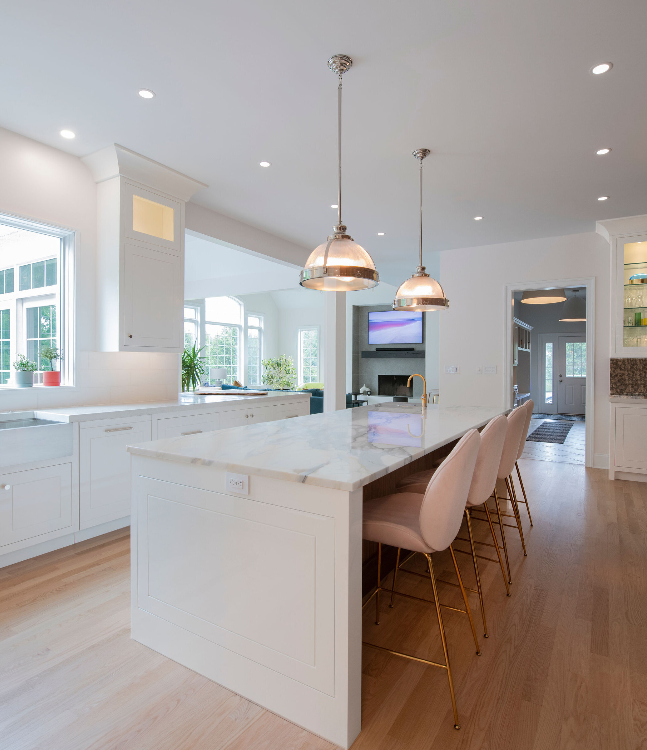  view of larger updated island in kitchen with white finish,, natural stone top, pink stools, single modern light fixture 