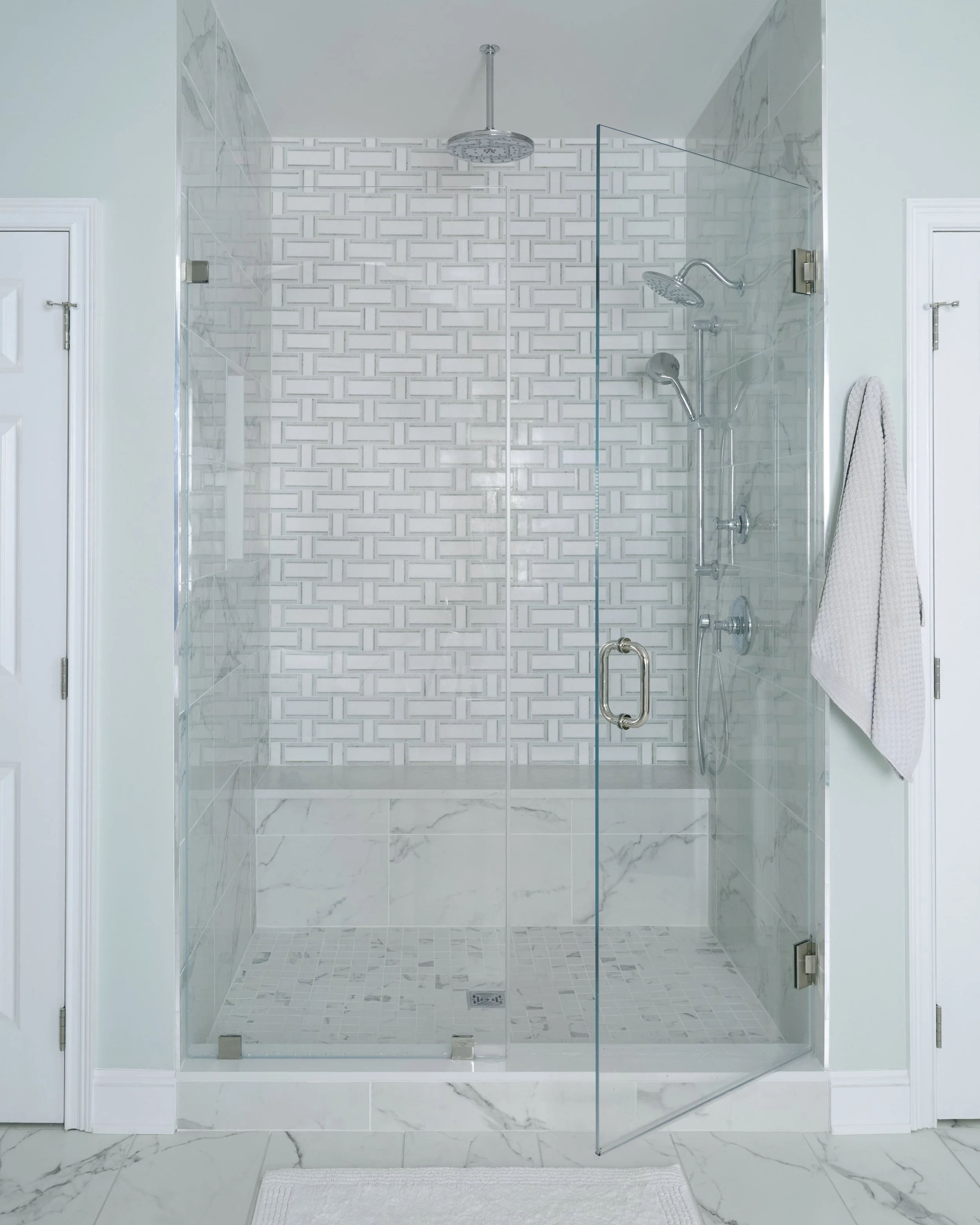 light bright airy clean sleek soothing primary bathroom with double vanity, elegant chandelier, patterned drapery, and free standing soaking tub. this image shows marbled and tiled shower in gray and white