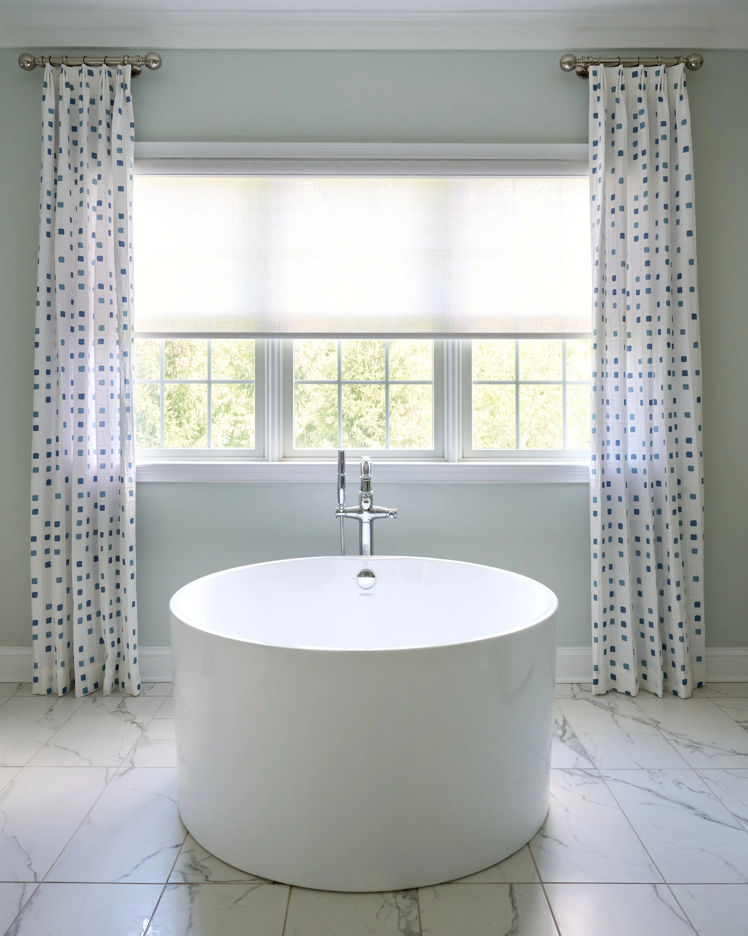 light bright airy clean sleek soothing primary bathroom with double vanity, elegant chandelier, patterned drapery, and free standing soaking tub