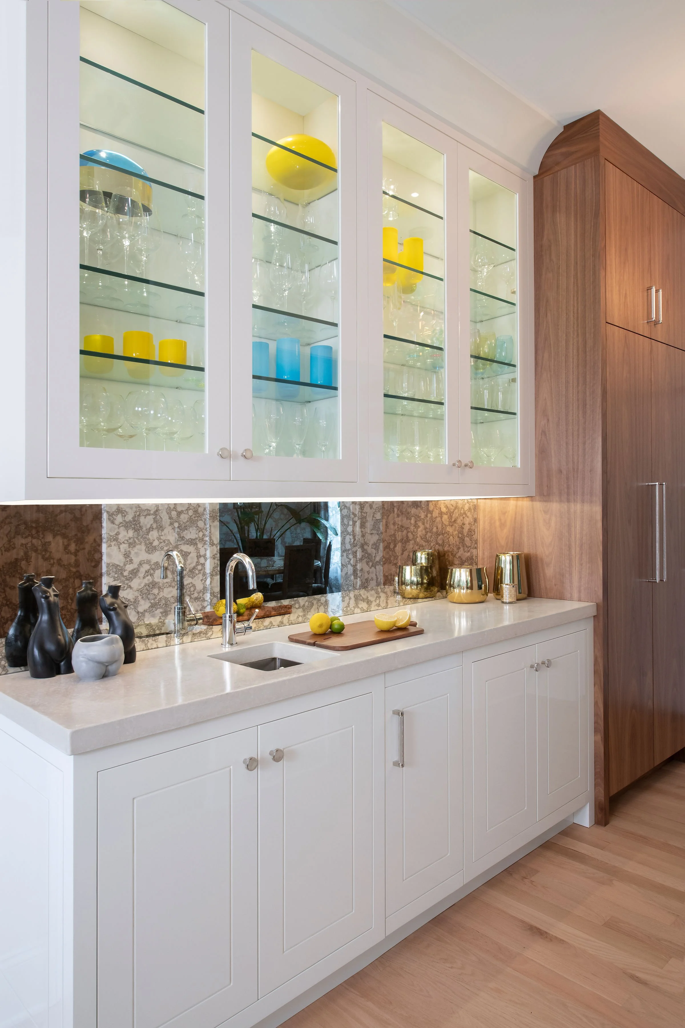 custom wine bar in contemporary and bright kitchen with custom white and wood cabinets, white island, natural stone countertops, pendants, light boxes, gold zip drain, wolf range, double oven, coffee compartment, hidden microwave,  hardwood floors,  