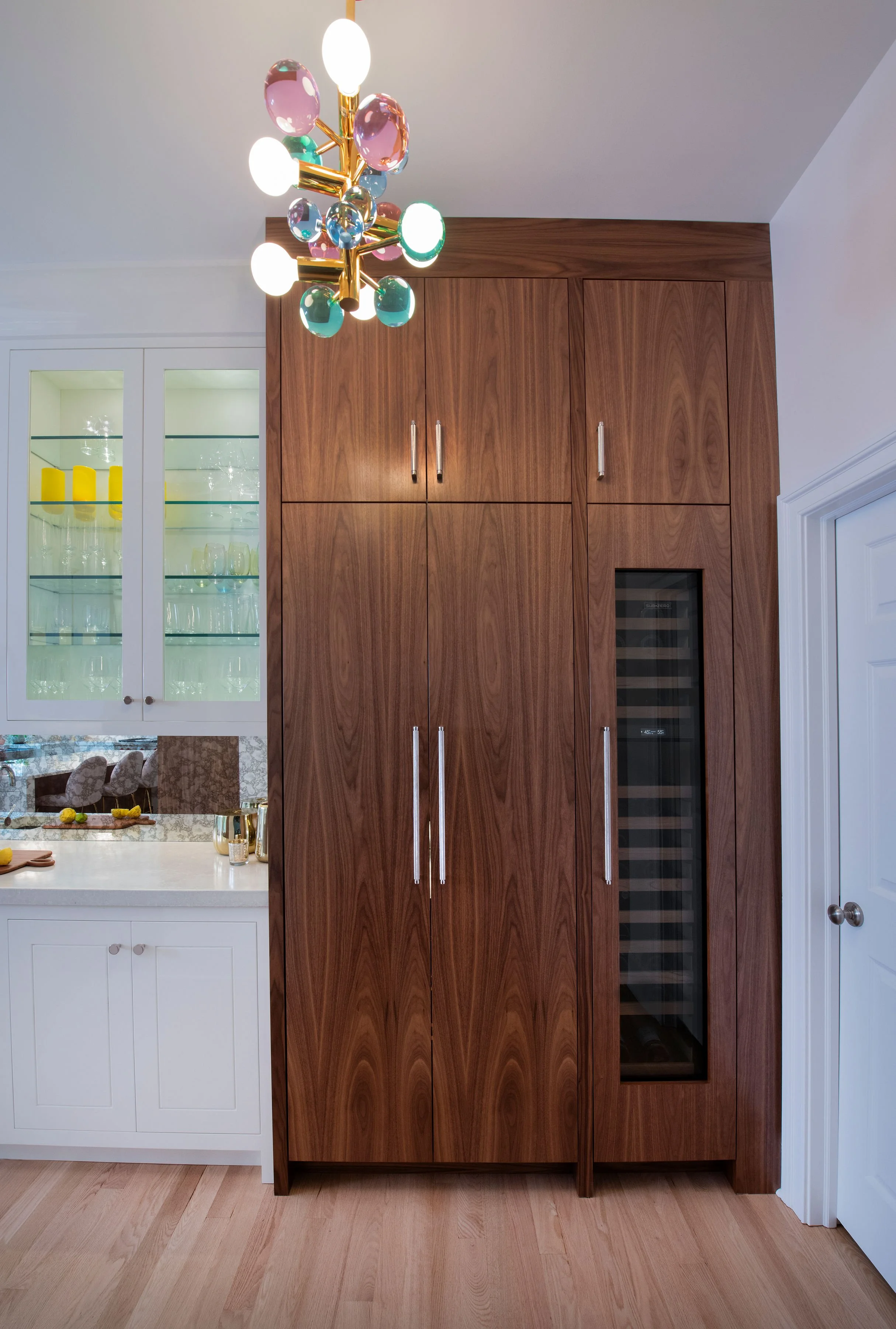 custom wine bar in contemporary and bright kitchen with custom white and wood cabinets, white island, natural stone countertops, pendants, light boxes, gold zip drain, wolf range, double oven, coffee compartment, hidden microwave,  hardwood floors,  