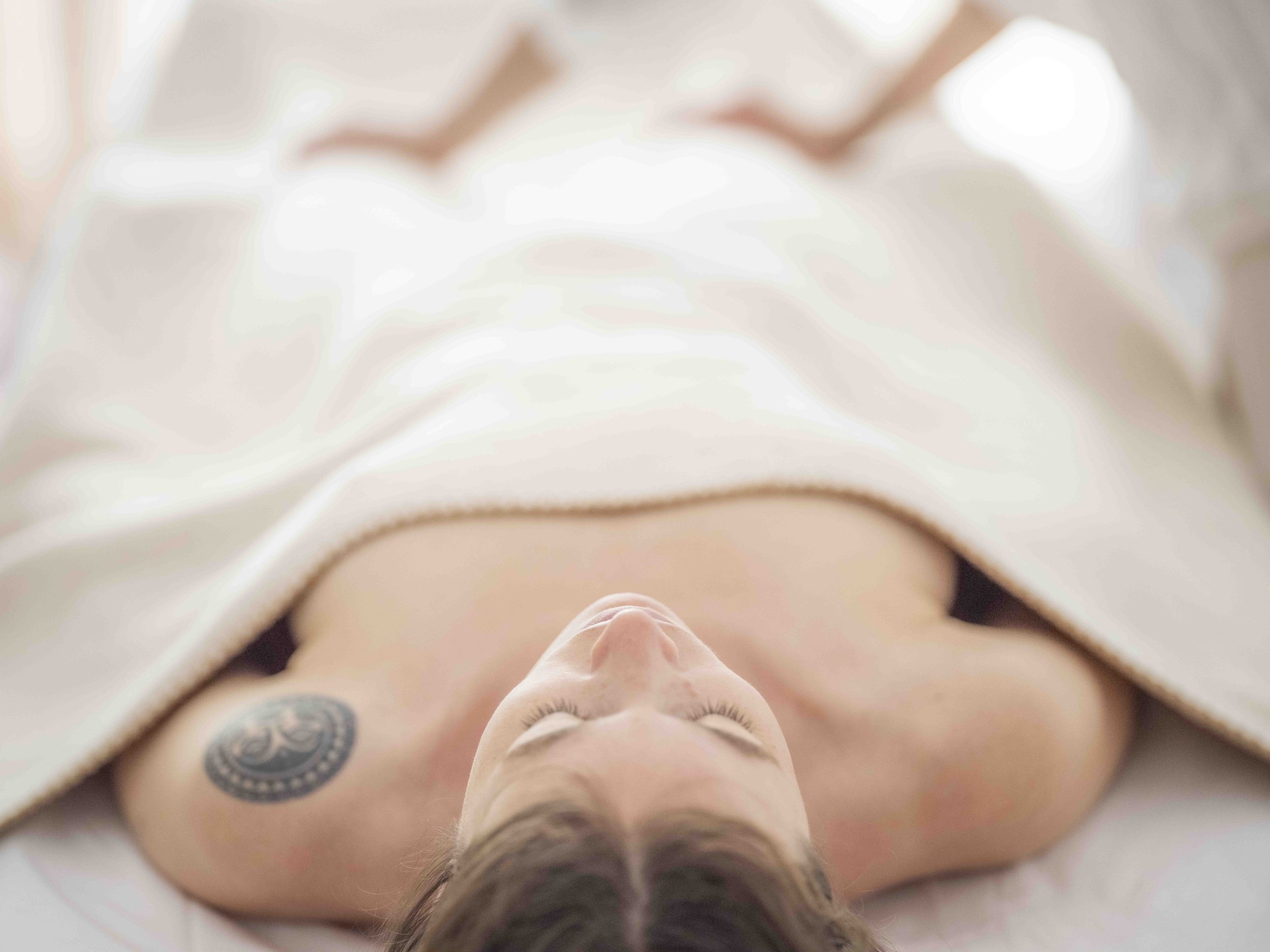 A woman lying in bed with the blanket pulled up, seen from above, with her eyes closed and her face relaxed.