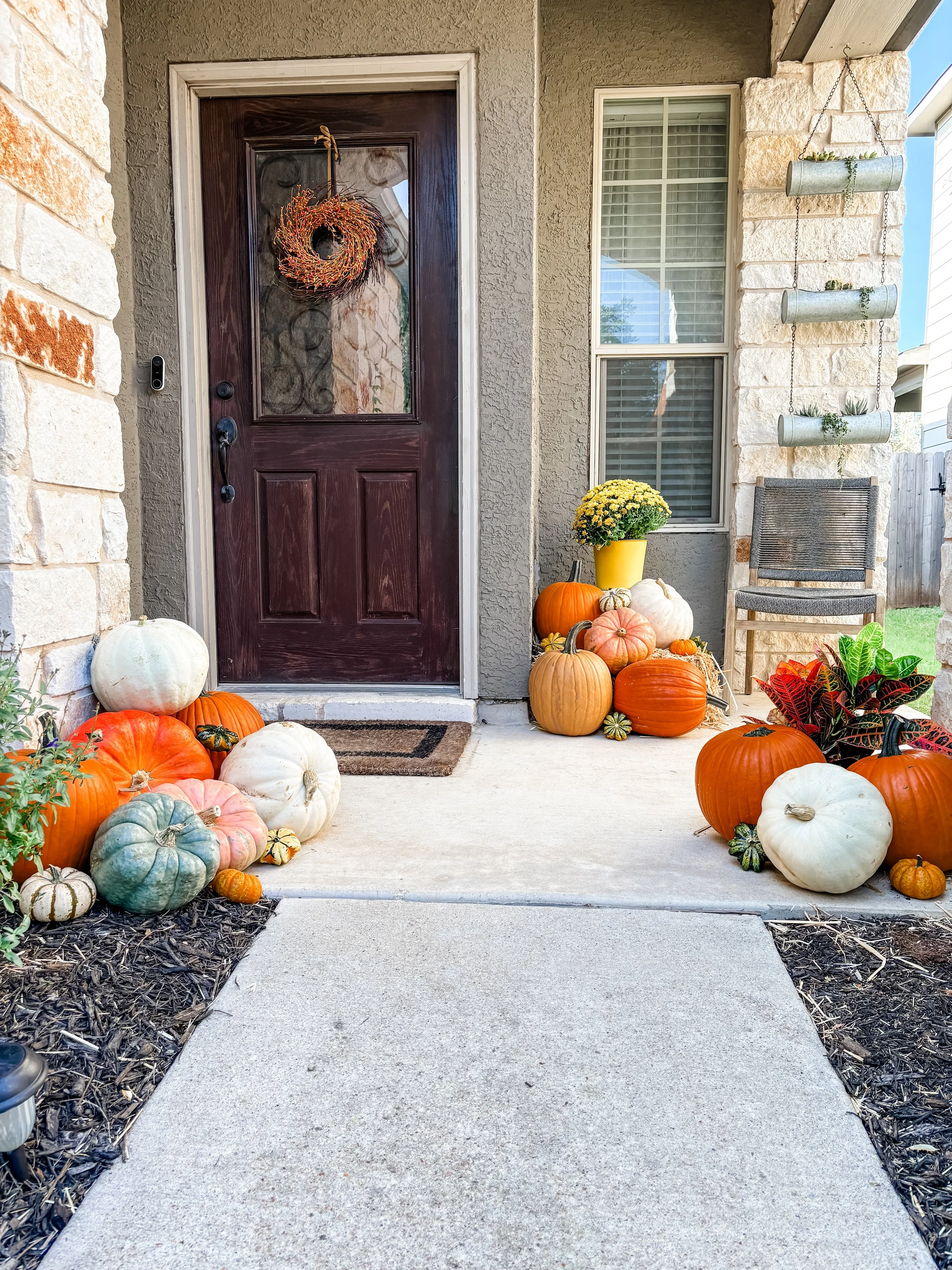 Decorated front porch with pumpkins, gourds, and fall flowers arranged around the entrance door for autumn or Halloween.