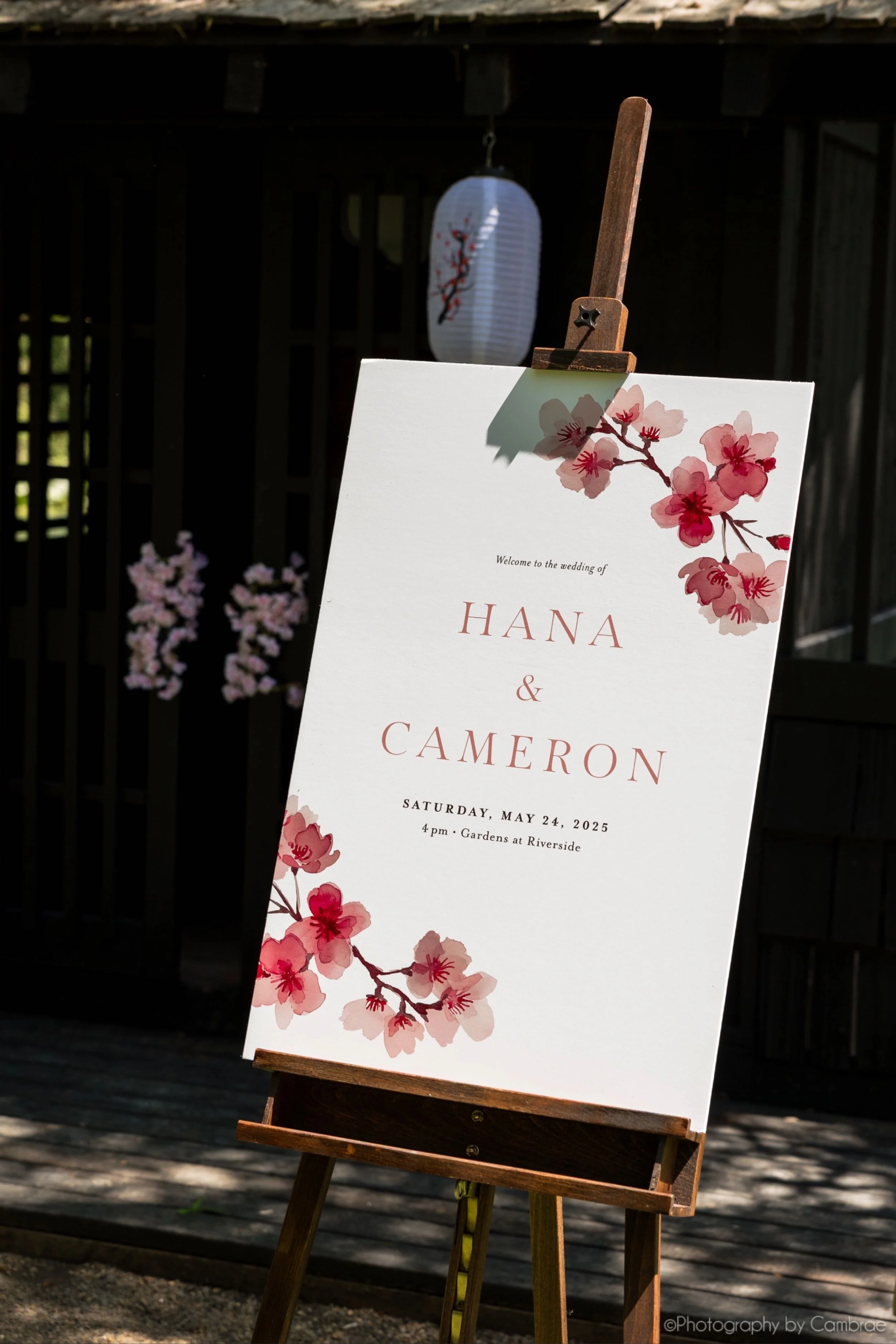 Wedding welcome sign with custom watercolor cherry blossom art sitting atop a wooden easel in a Japanese garden at the Gardens at Riverside wedding venue in Albany, Oregon