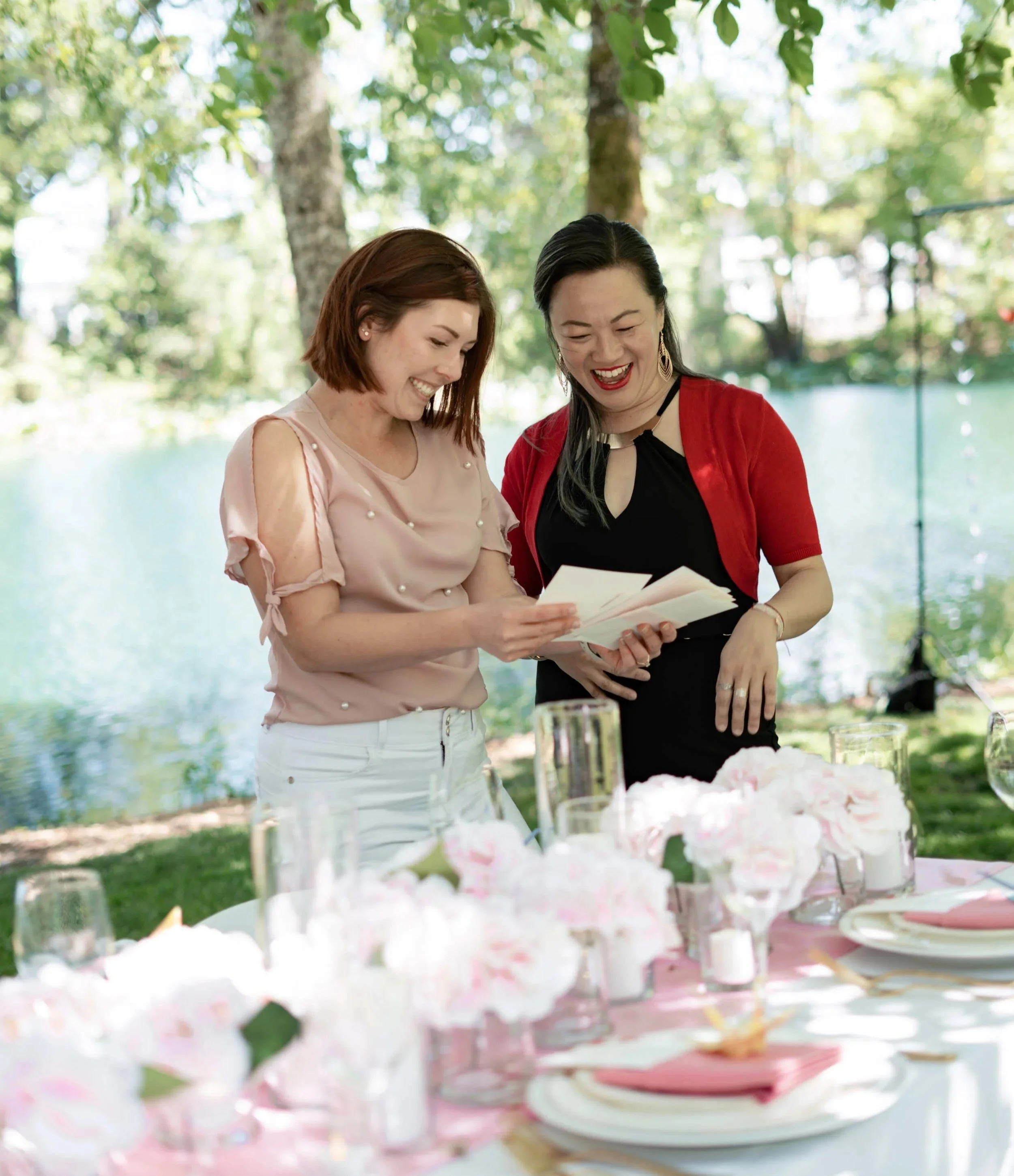 Michelle Roberts and wedding planner admiring beautiful custom wedding stationery with watercolor art of cherry blossoms at a wedding table setting at the Gardens at Riverside venue in Albany, Oregon