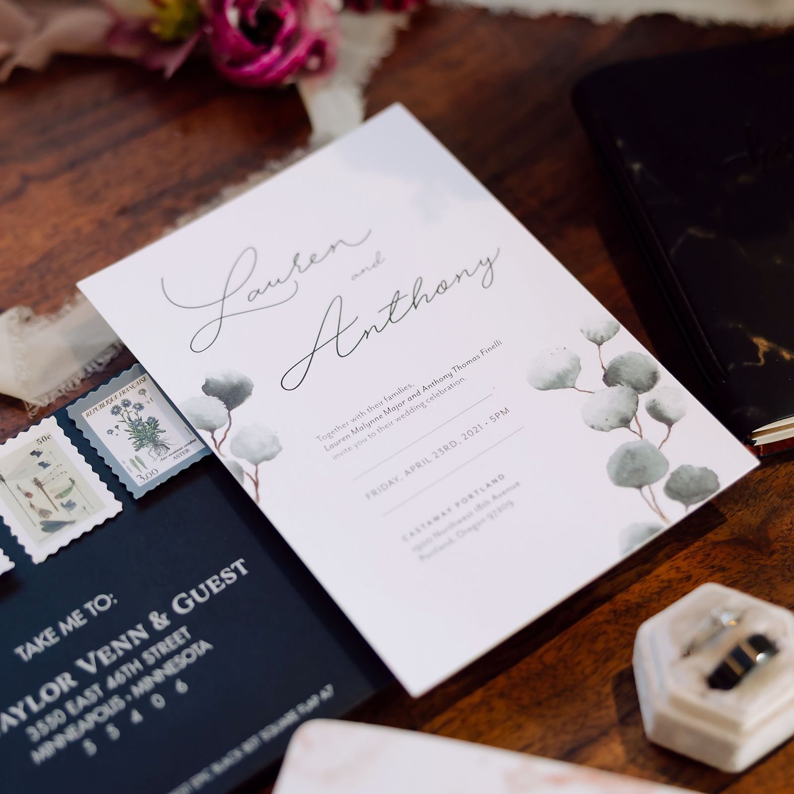 Wedding invitation with watercolor eucalyptus sitting on top of a dark envelope with vintage stamps