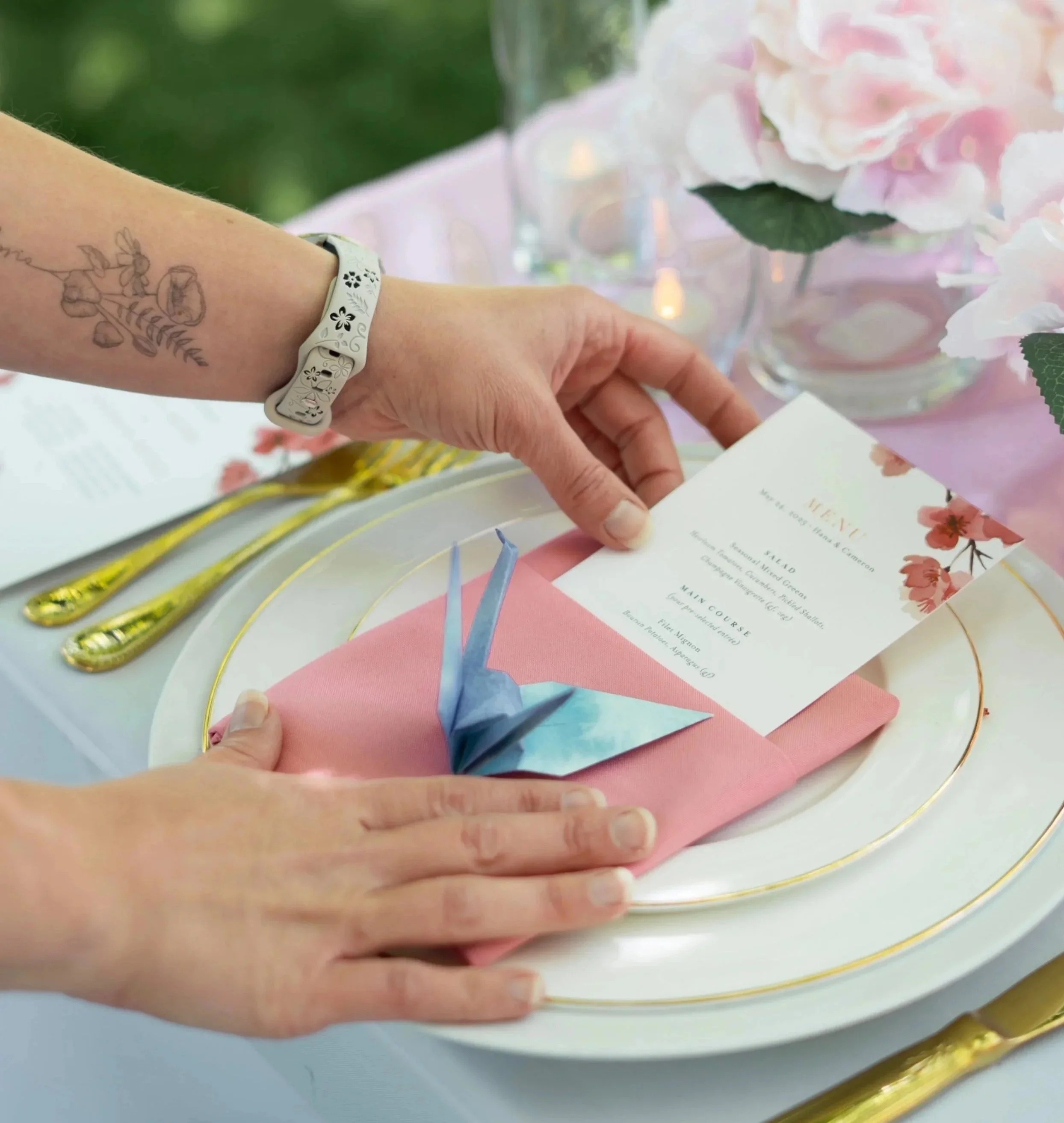 Stationer placing wedding dinner menu with watercolor cherry blossoms inside of a dinner napkin