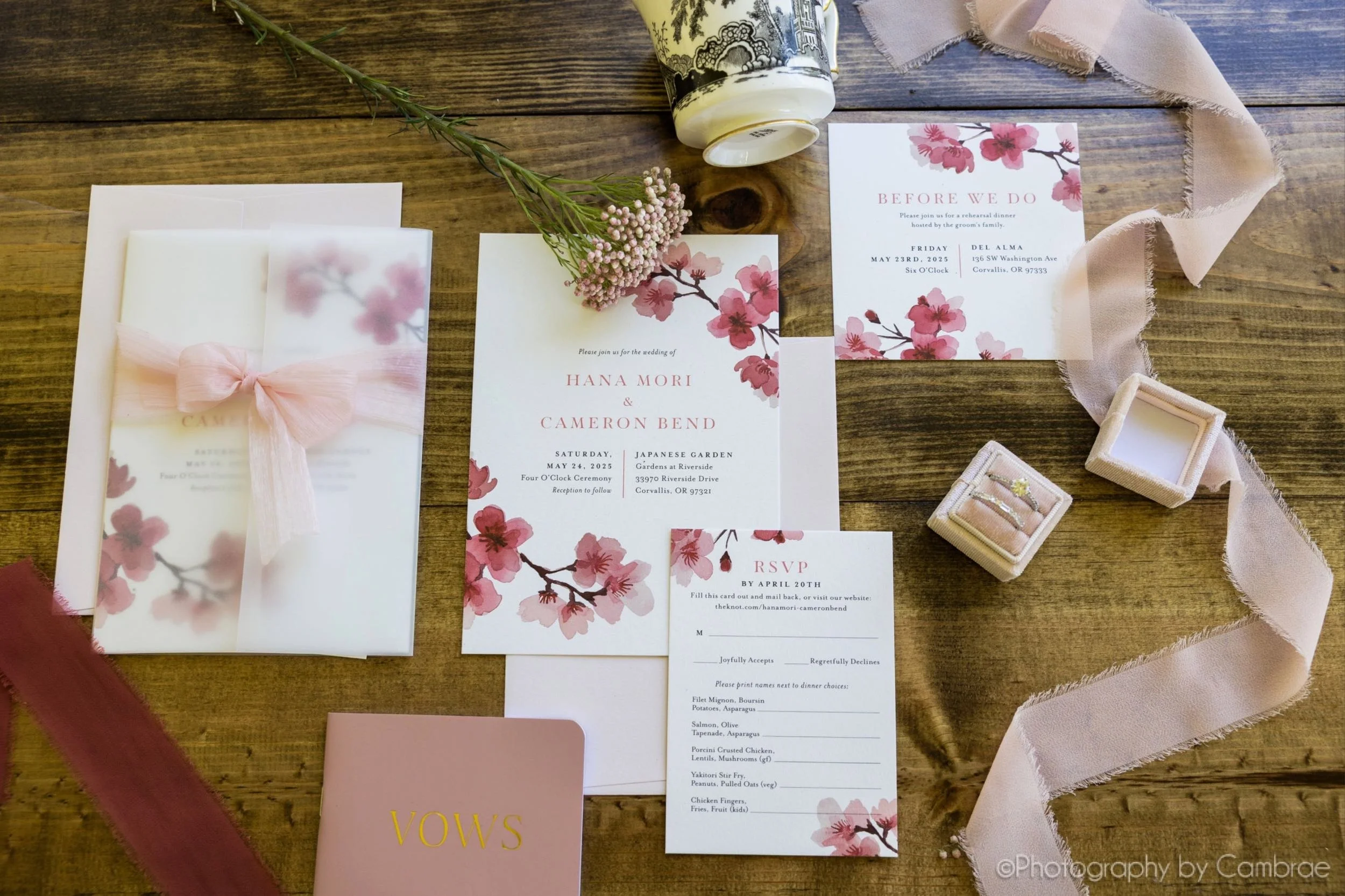 Custom watercolor art invitation suite flat lay with cherry blossom designs and pink ribbon