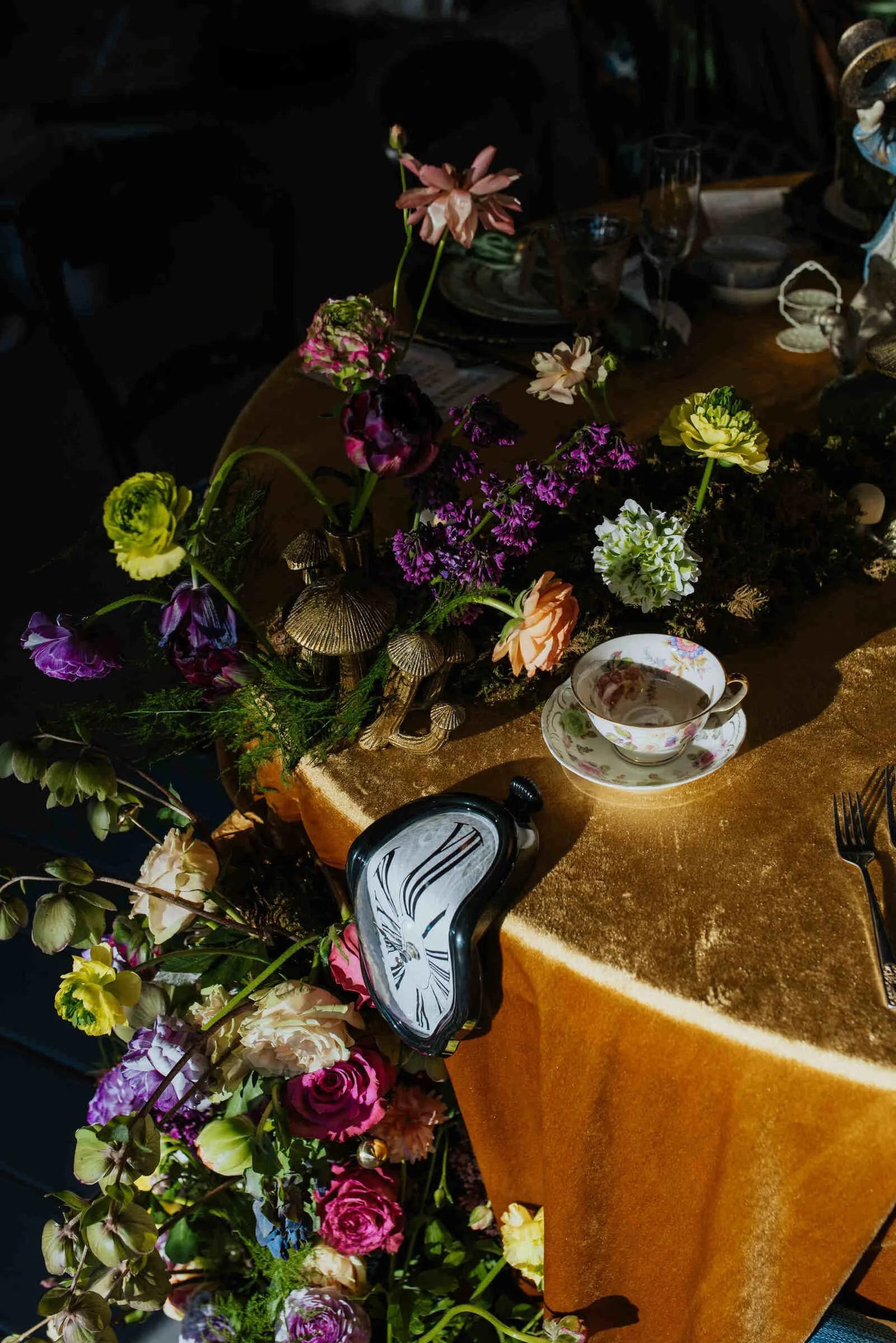 Alice in Wonderland alternative wedding theme tea party table setting with teacup, melting clock and florals cascading over edge