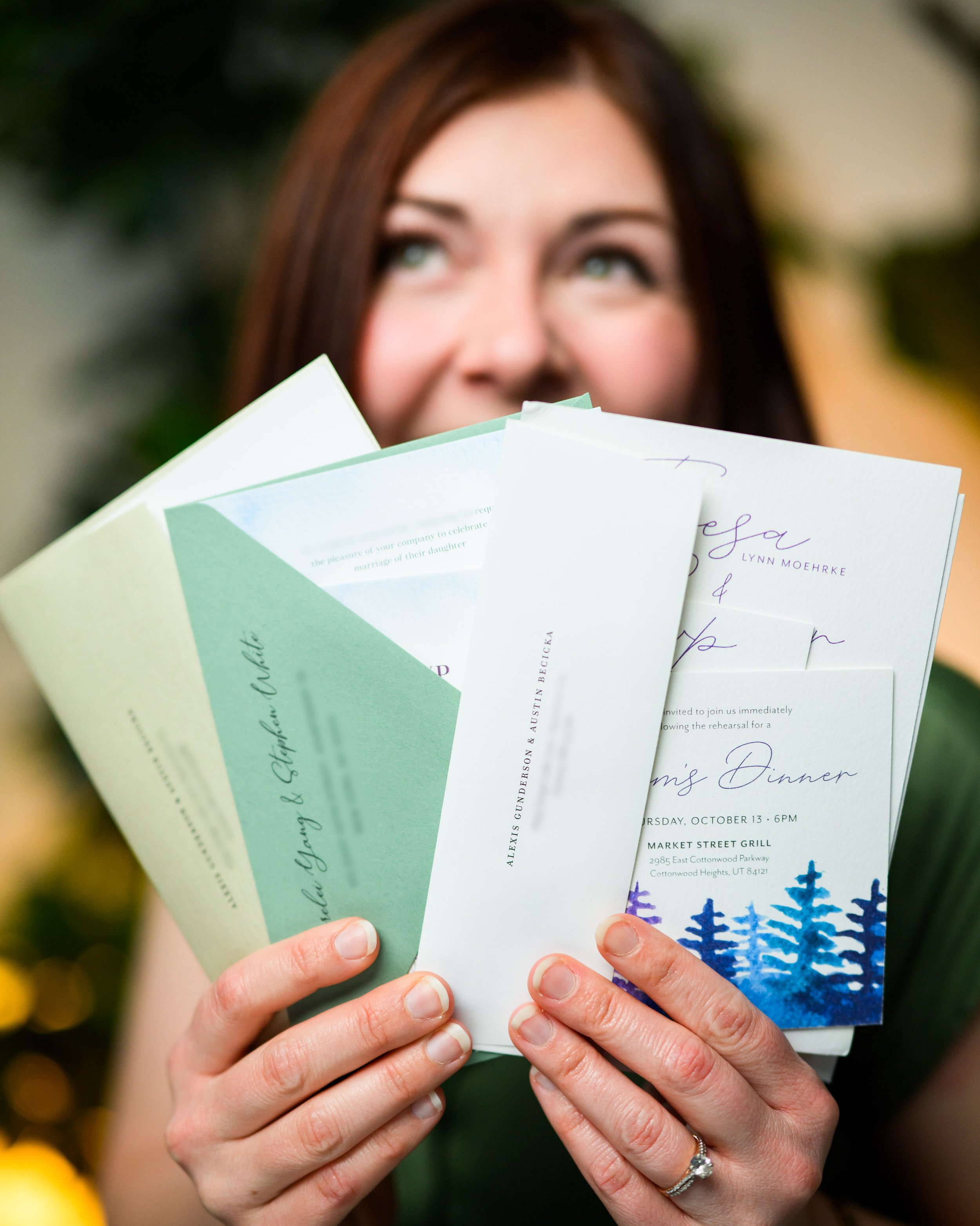 Michelle Roberts holding watercolor wedding invitations in front of her face, partially covering her face, with only her eyes and hair visible.