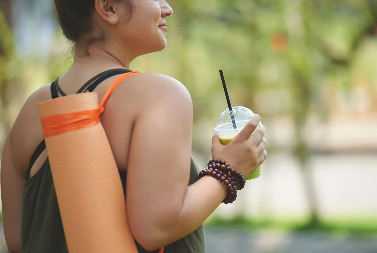 woman-drinking-juice-carrying-yoga-mat.jpg