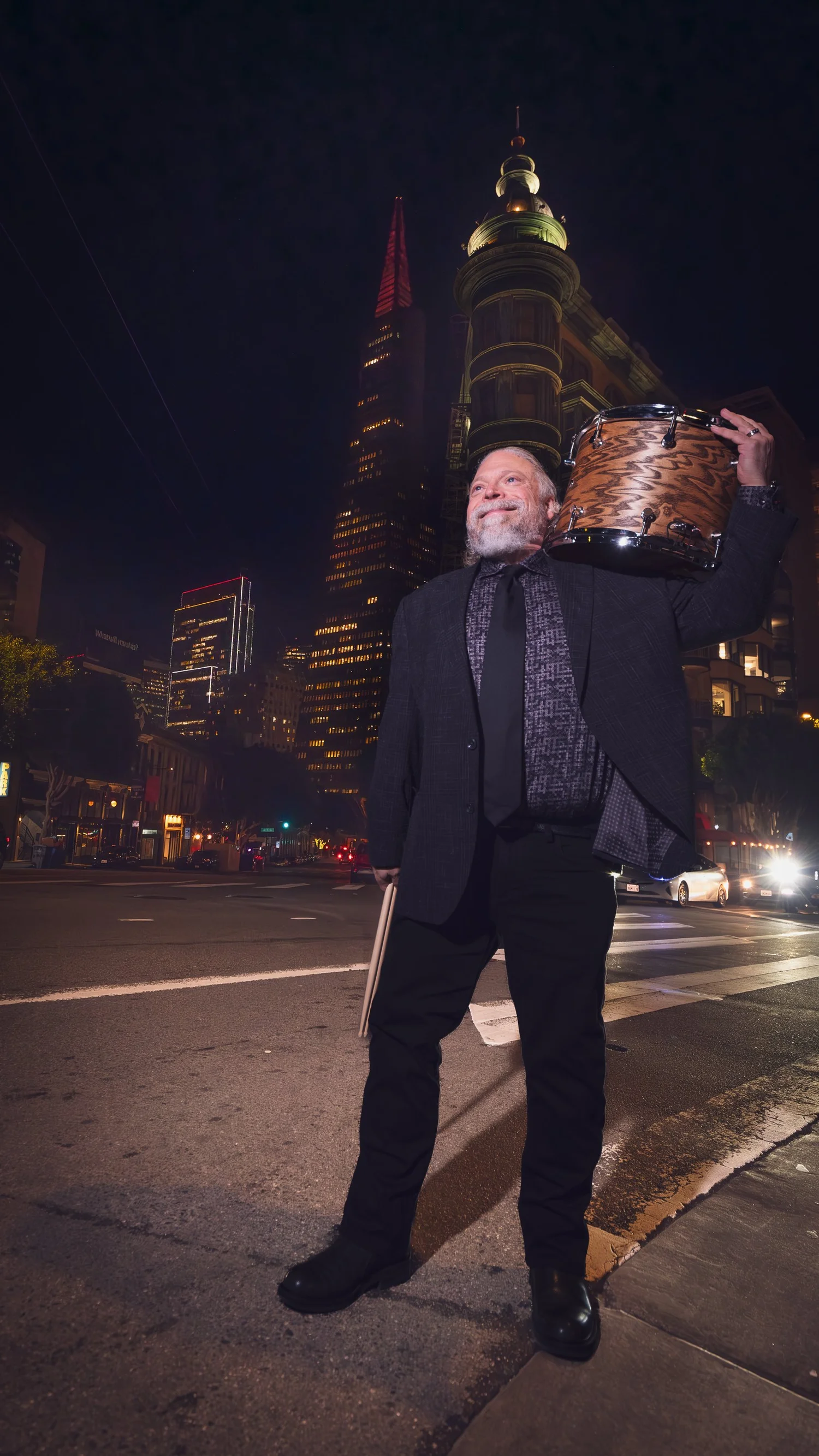 Chris Gamper holding a cymbal on a San Francisco street at night with the Transamerica Pyramid behind him