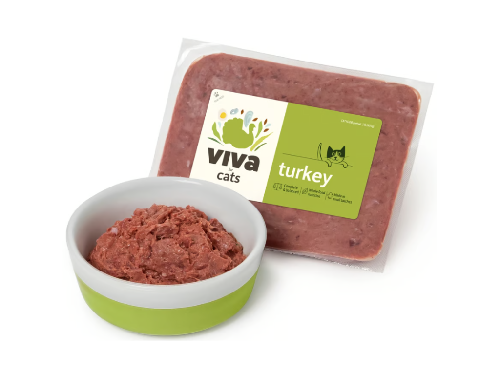 Packaged turkey cat food labeled "Viva Cats" next to a green and white bowl filled with wet cat food. The tone is clean and appetizing.