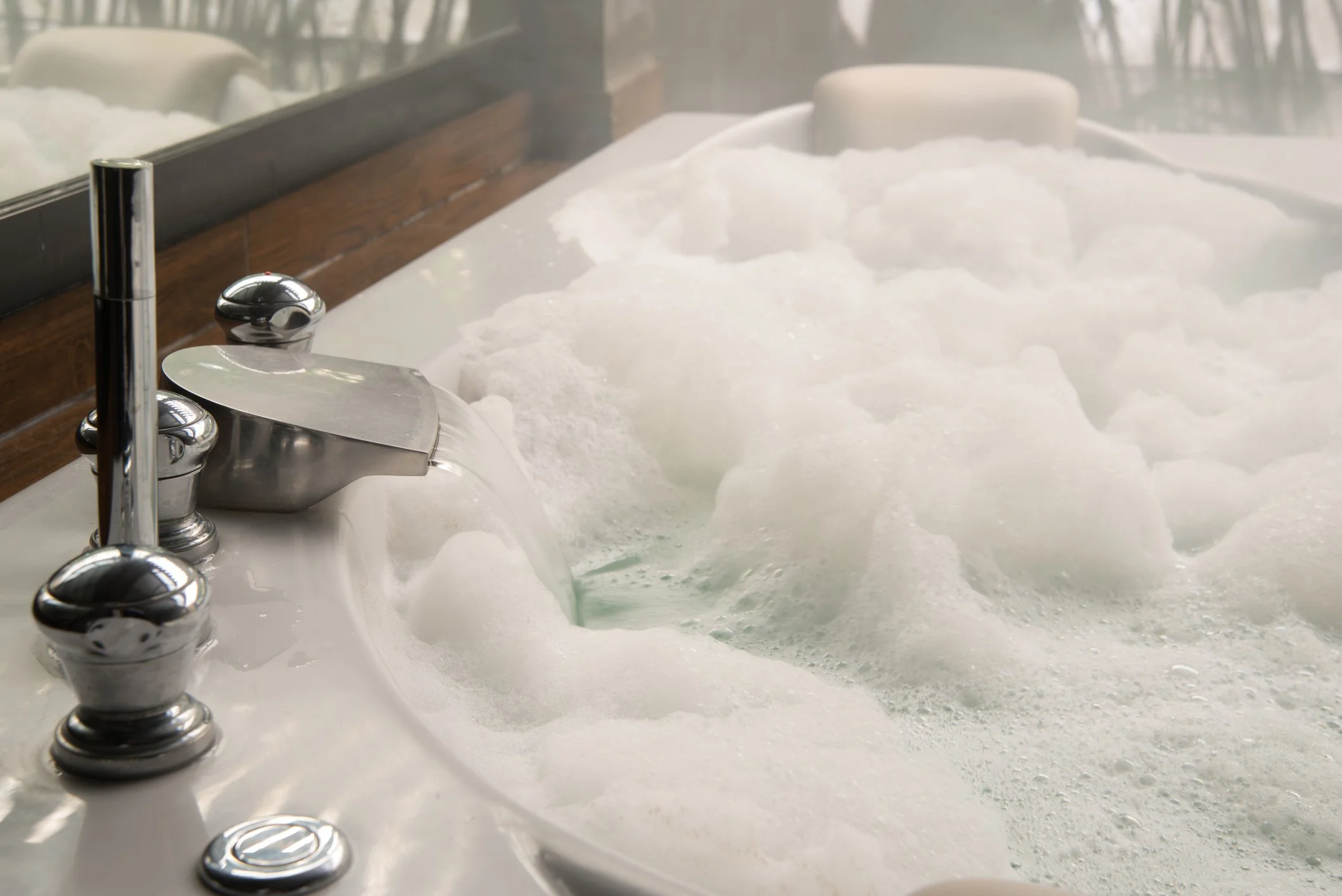 A hot bath with foam on the water, chrome faucet, and wooden panelling in the background.