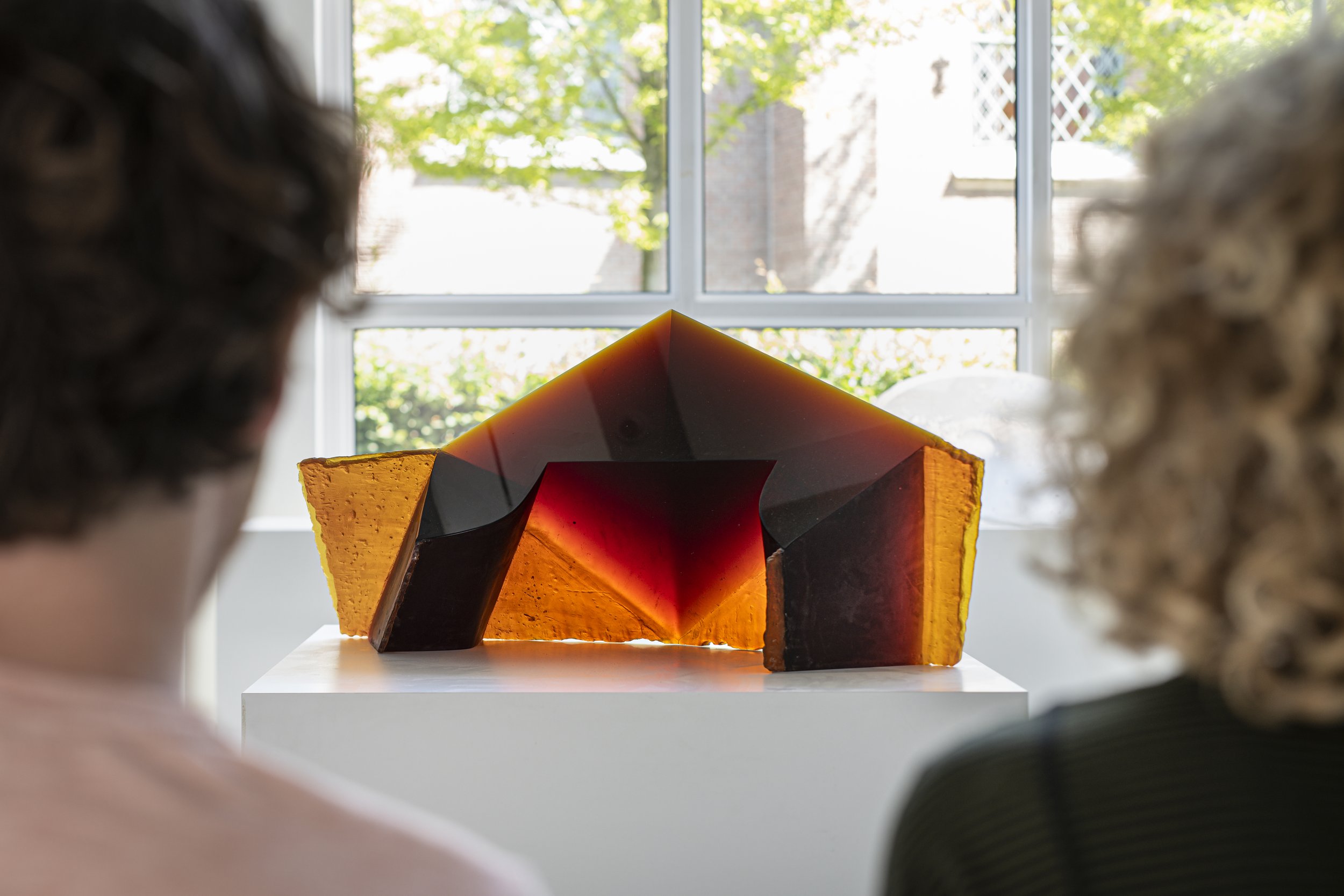 Twee personen van de achterkant die kijken naar een glazen sculptuur op een sokkel
