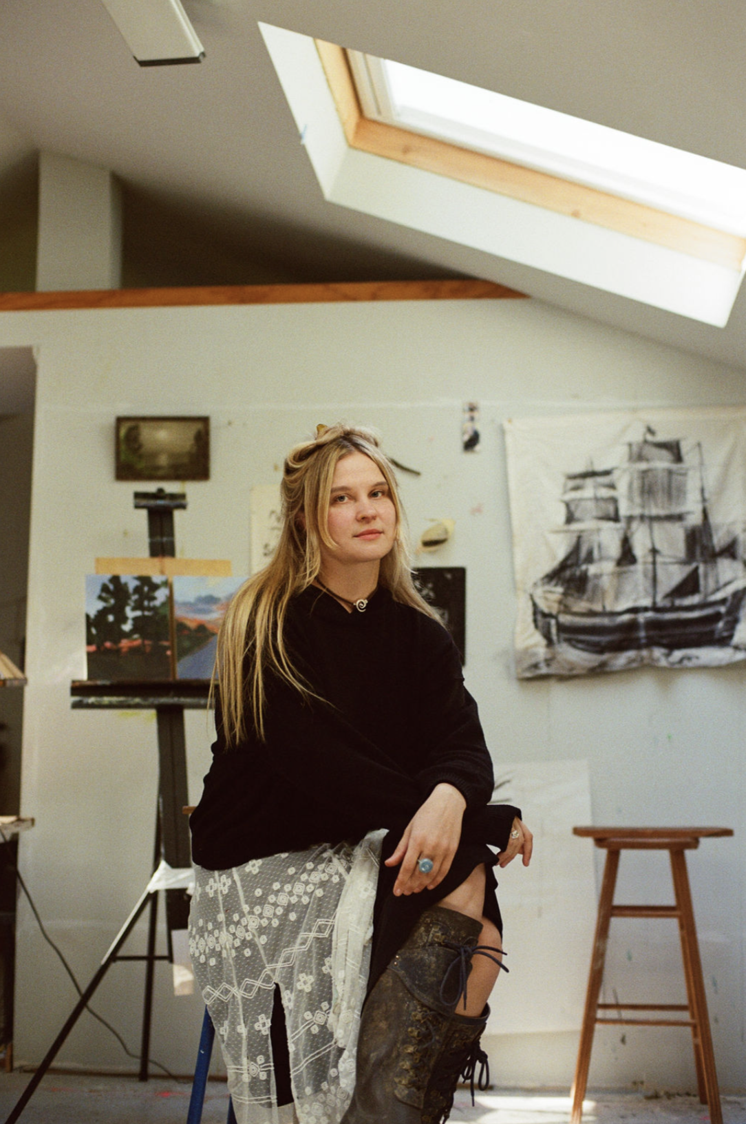 Woman posing in an art studio surrounded by paintings and a skylight