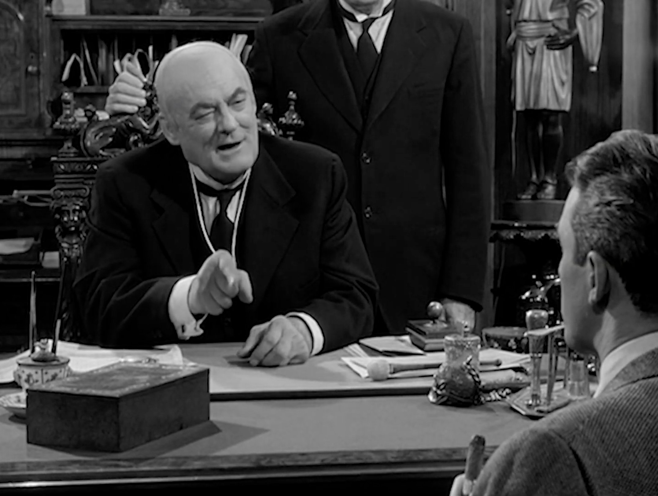 Power on Display In this shot, the camera gives Potter the visual high ground: he’s centered, well-lit, and leaning toward us with that pointed finger, while George is reduced to the back of a head in the foreground. The framing, depth of field, and Potter’s relaxed posture sell him as confident, reasonable authority—which is exactly the danger. Filmmaking reminds us here that manipulative people rarely look like villains; they often present as calm, certain, and in control while pushing you toward a compromise you’ll regret.