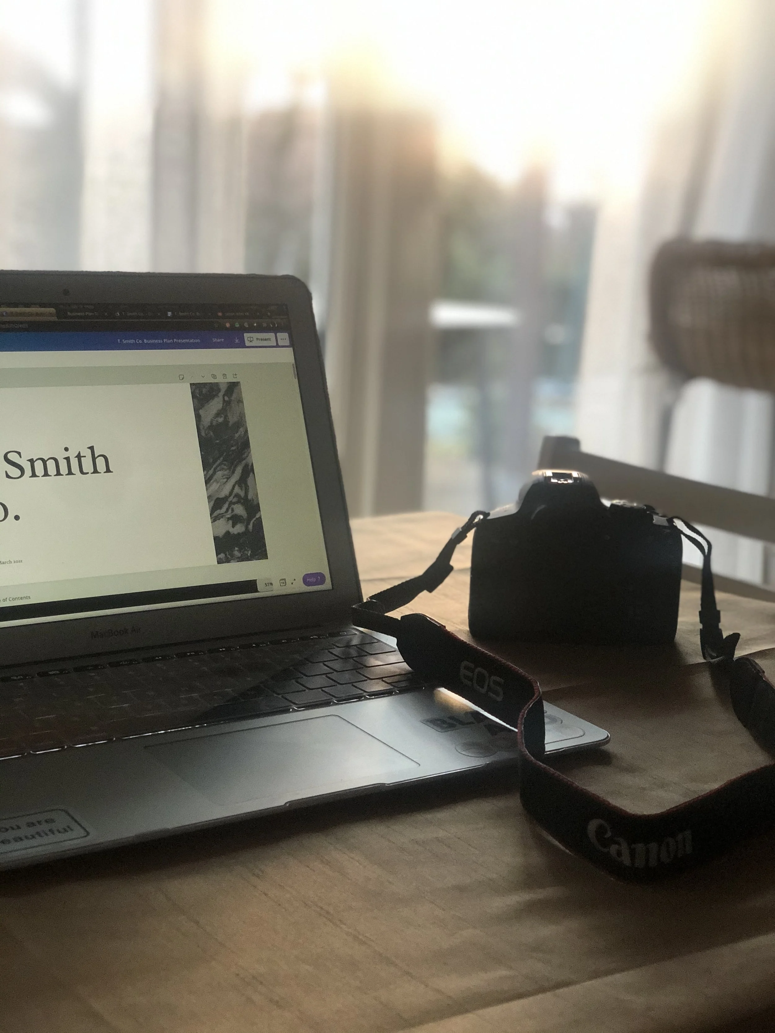 A laptop displaying T. Smith Consulting work and a camera sitting on a table on a sunny day